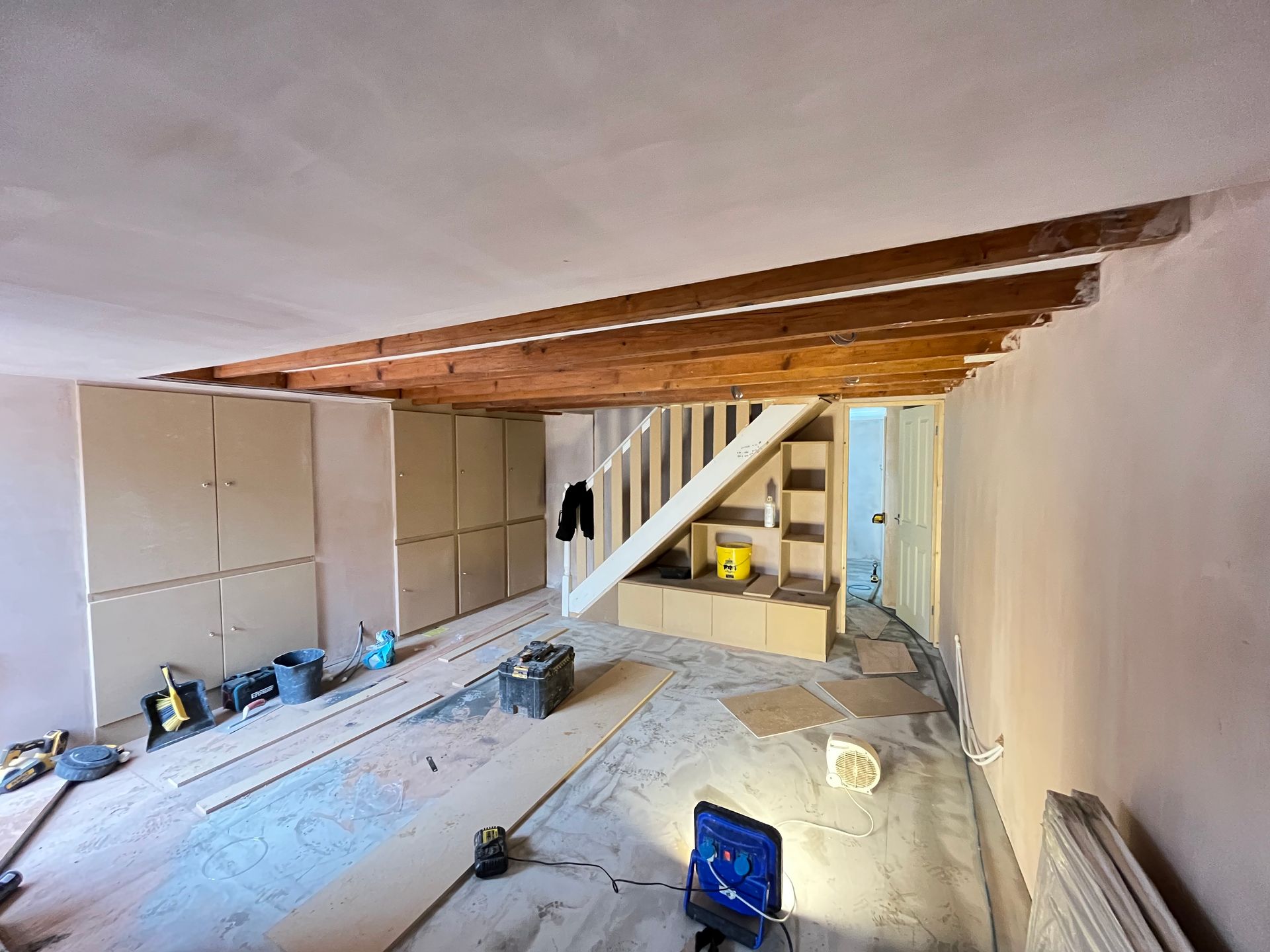 Renovated interior, exposed beams, stairwell, built-in storage, tools on the floor, drywall, and construction materials.