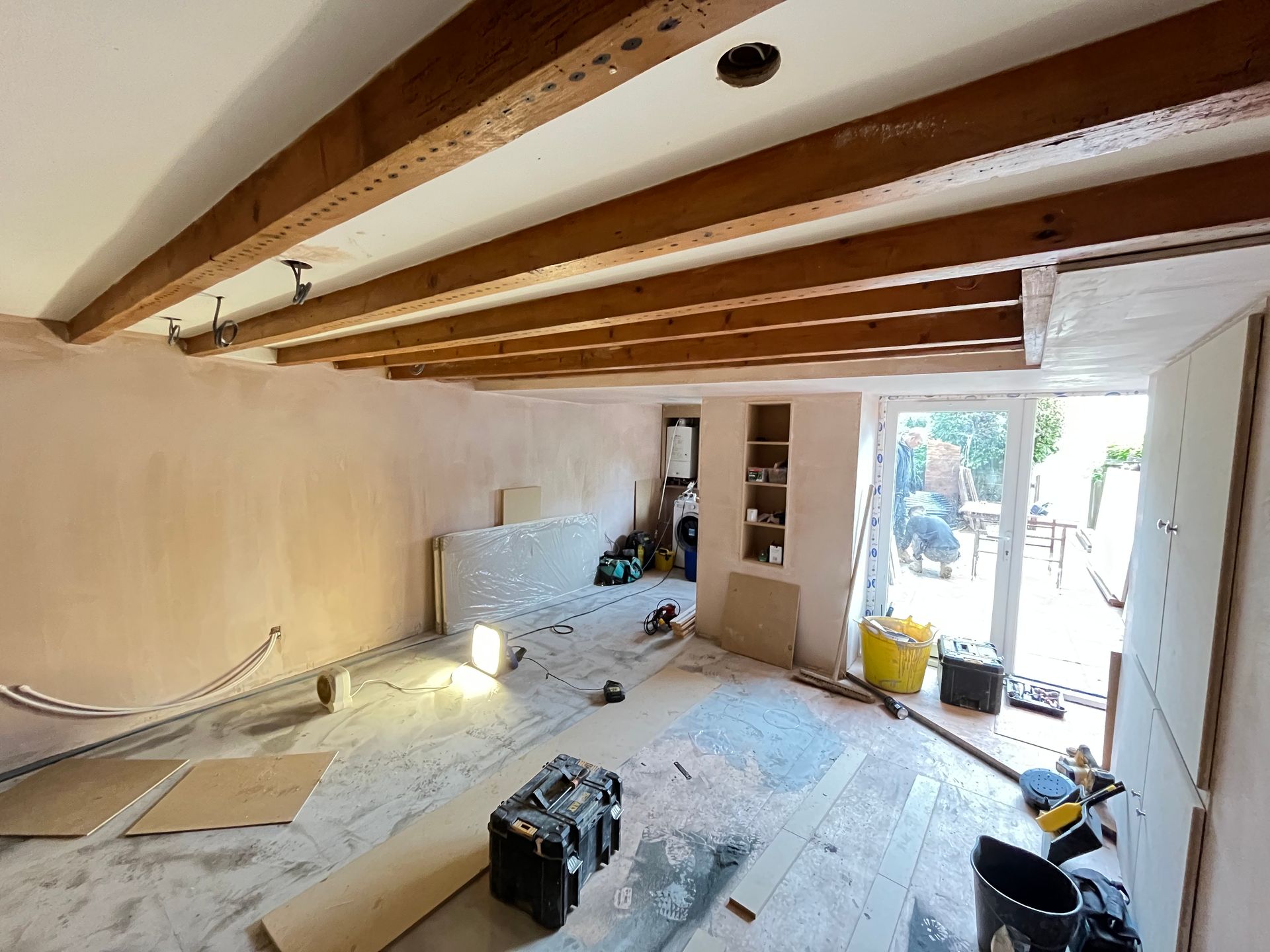 Room under construction, exposed wooden beams, pink walls, debris on floor, open door to garden.