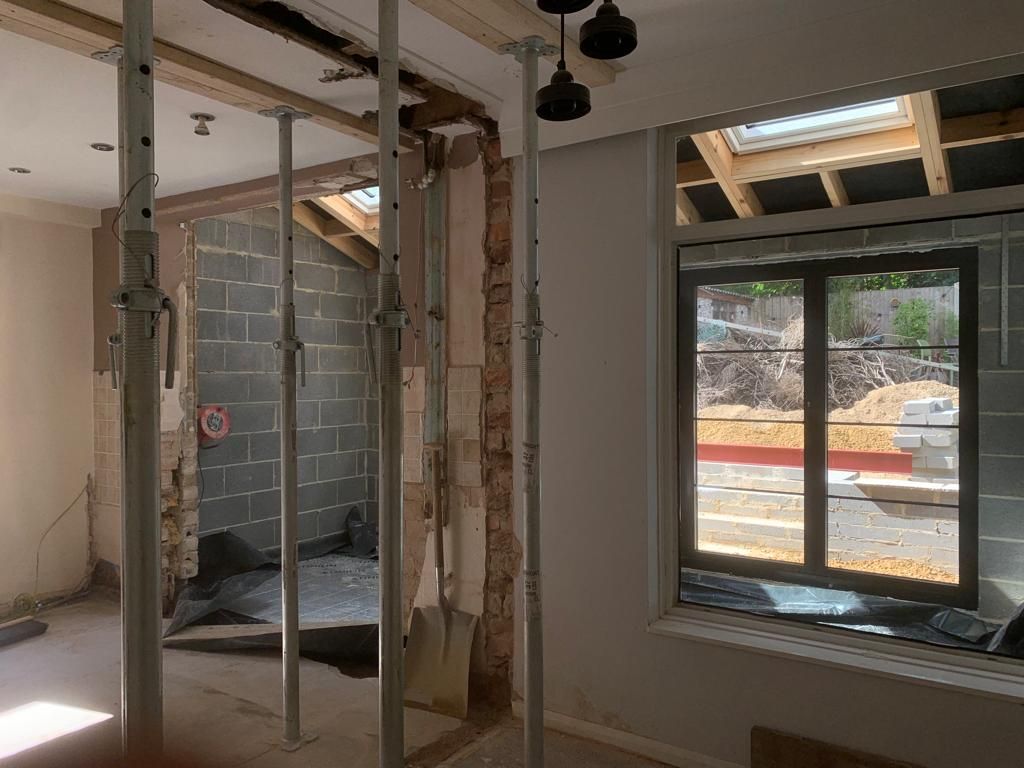 Interior renovation in progress; temporary support beams, exposed walls, and window view to construction site.