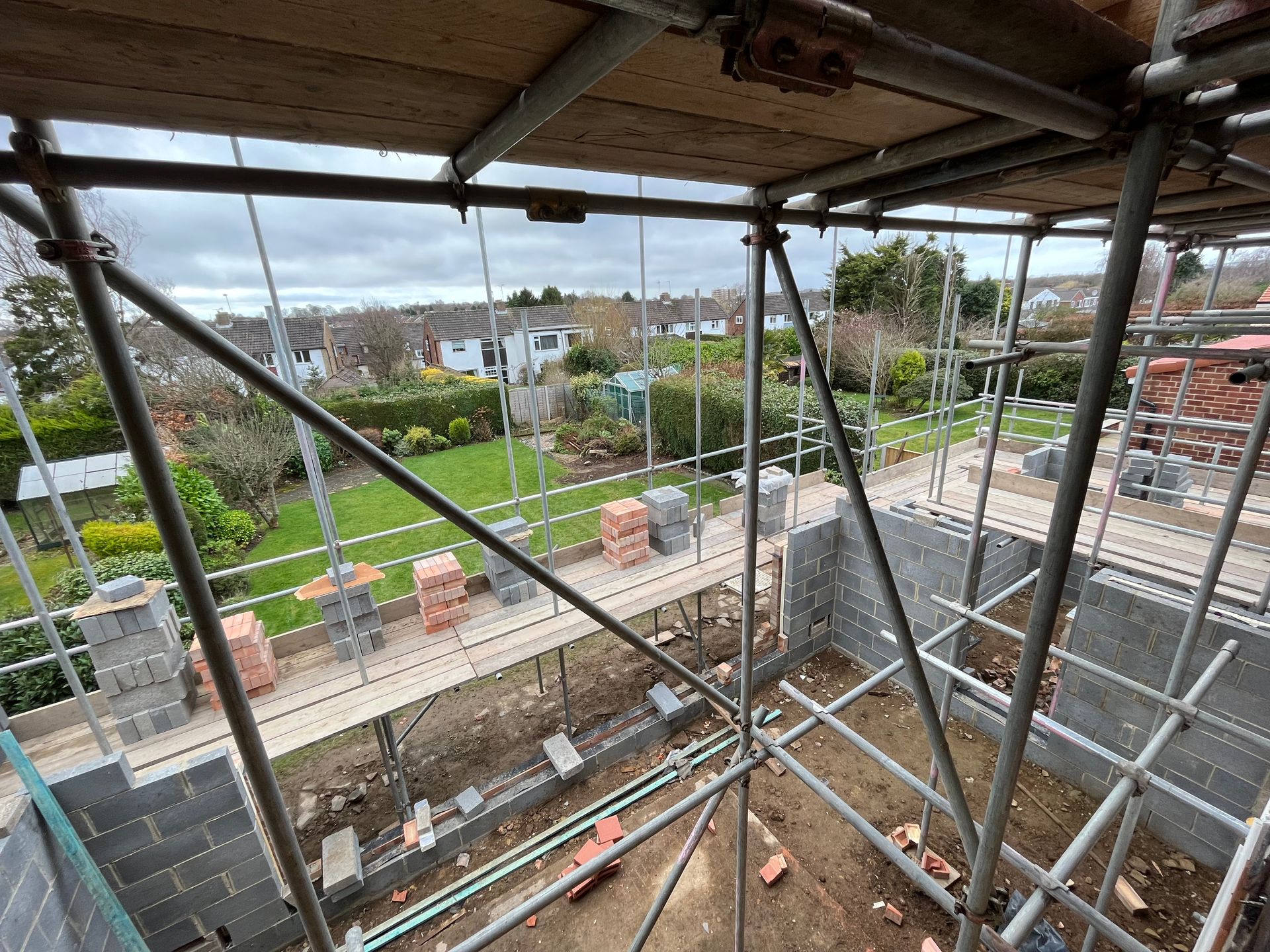 Scaffolding on building under construction, overlooking backyard with houses on a cloudy day.