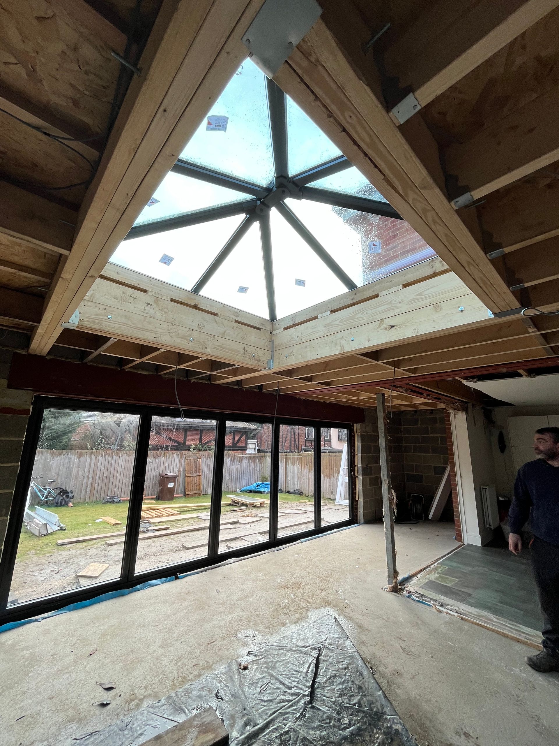 Interior view of a room under construction with large glass doors, a skylight, and exposed beams.
