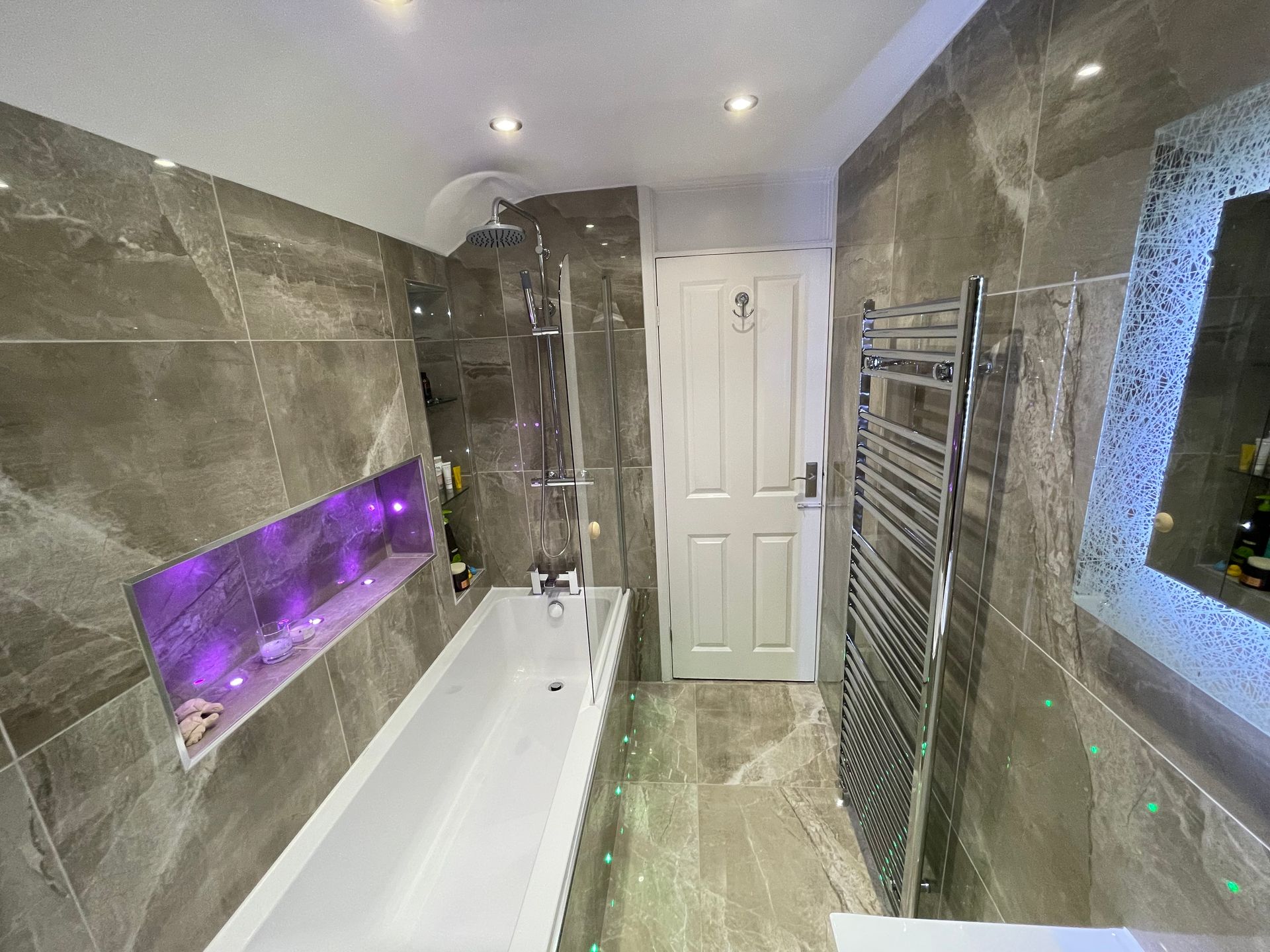 Modern bathroom with grey marble tiles, a white bathtub, and LED lighting.