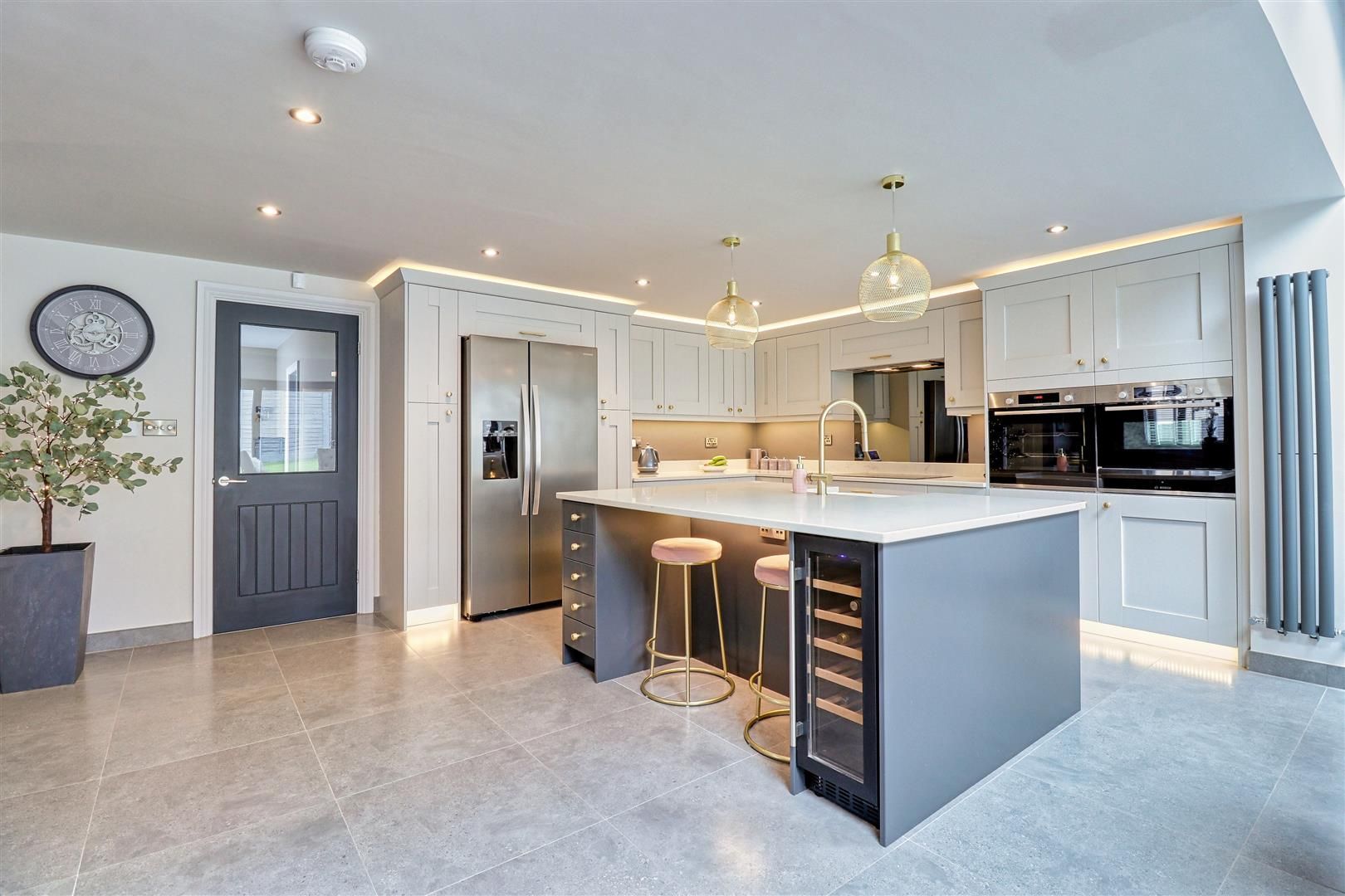 Modern kitchen with gray cabinets, stainless steel refrigerator, island with a wine cooler, and gold accents.