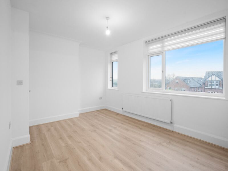 Empty, bright room with wood-look flooring, white walls, and a large window with a view of houses.