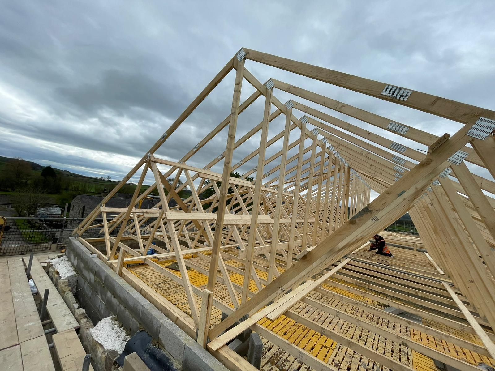 Wooden roof trusses being assembled on a building under a cloudy sky.