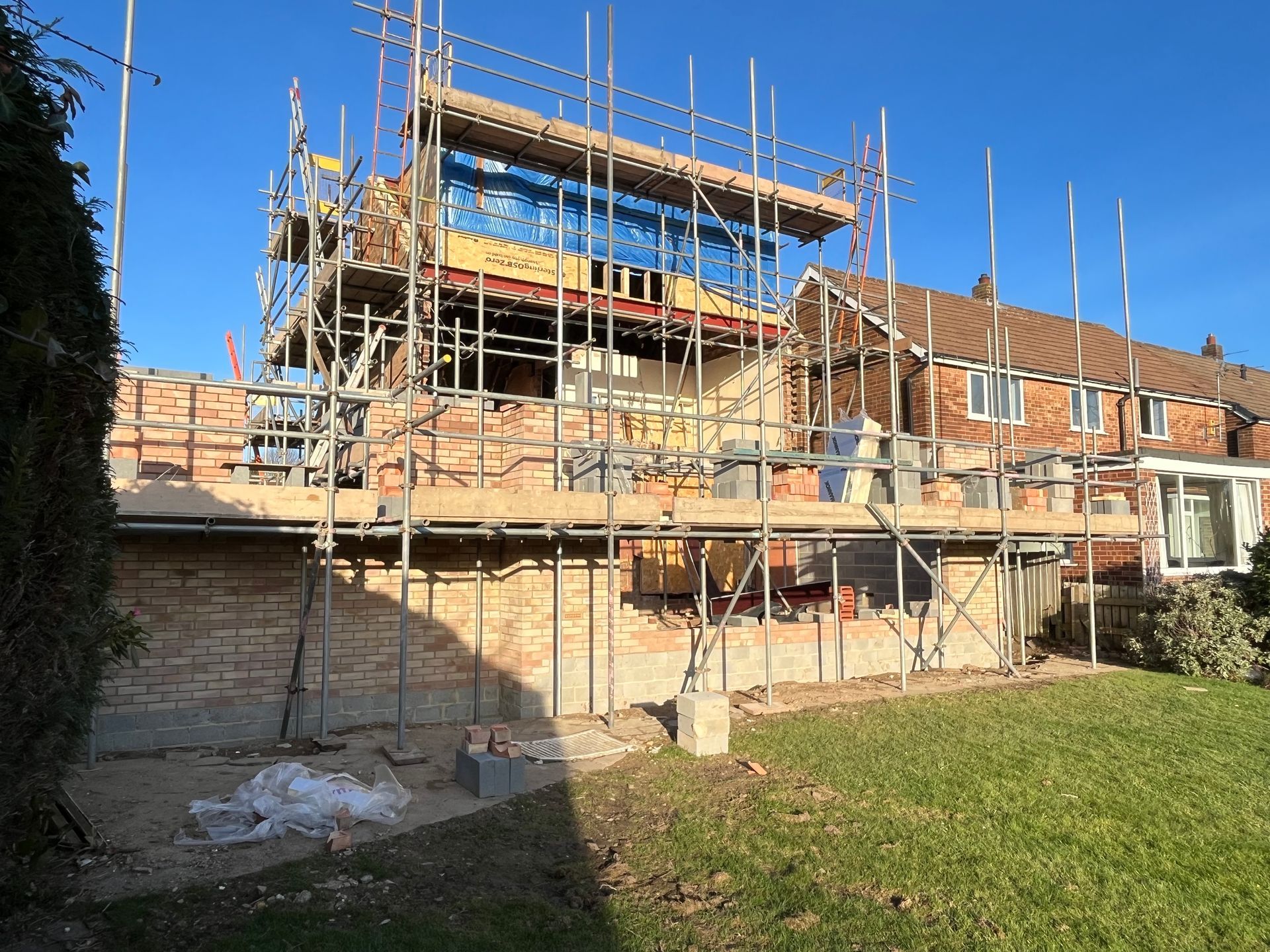 House undergoing renovation; brickwork, scaffolding, grass lawn, blue sky.