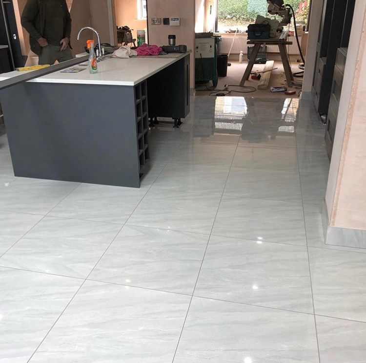 Gray kitchen island with white countertop in a room with light-colored tile flooring and a person in the background.