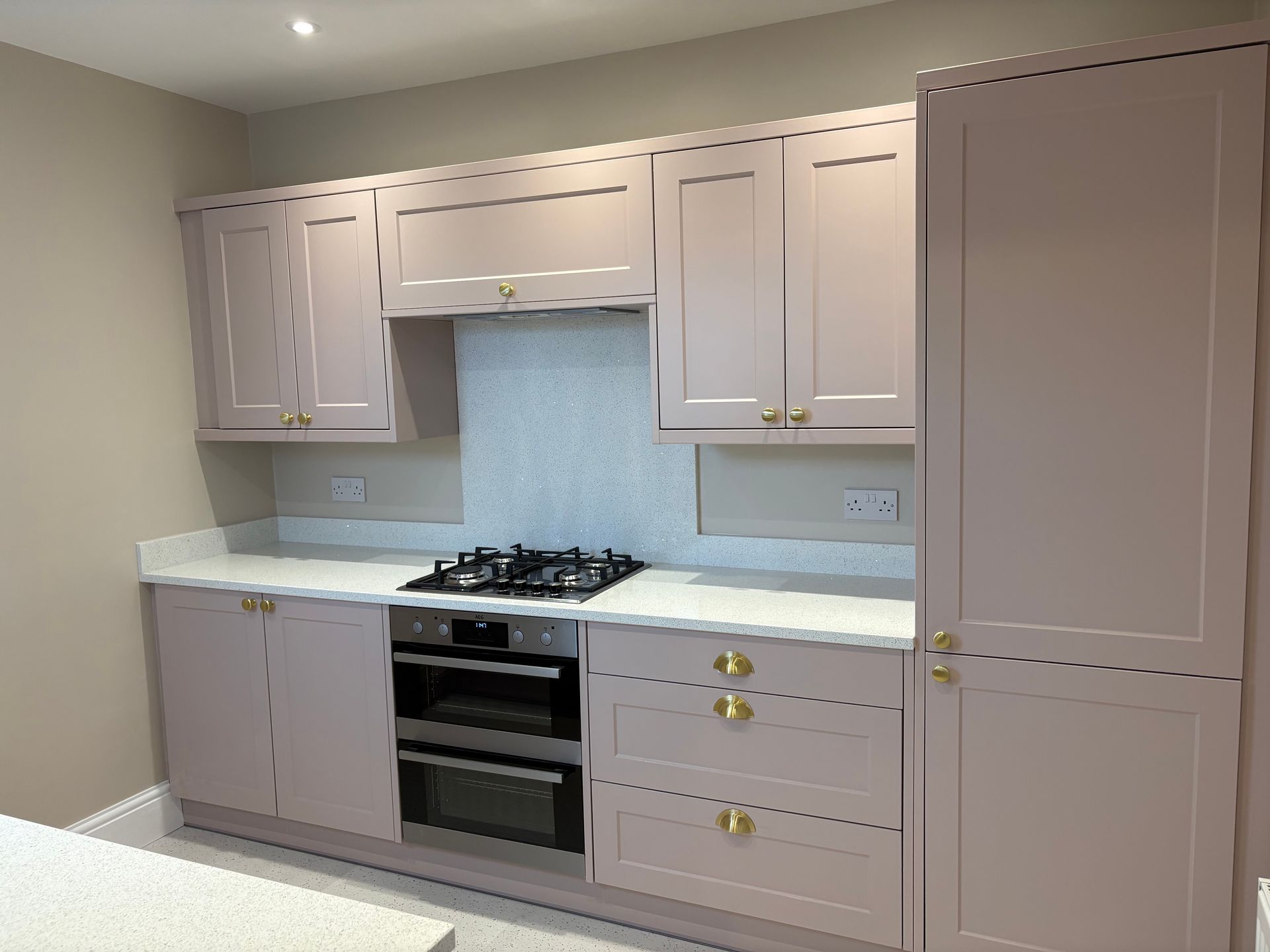 Pink kitchen cabinets with white countertops and gold hardware.