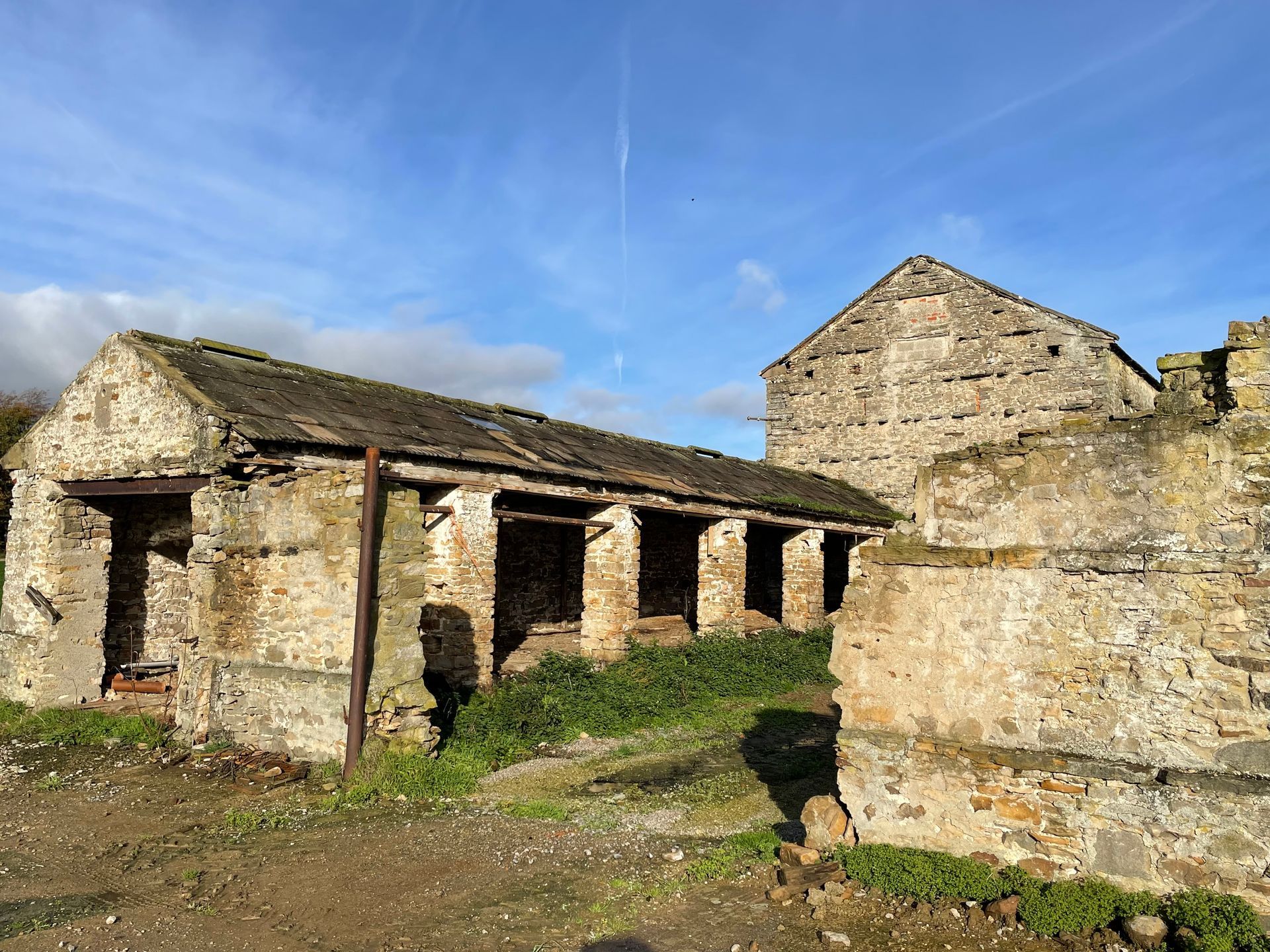 Ruined stone buildings with open doorways sit under a blue sky, surrounded by green grass.