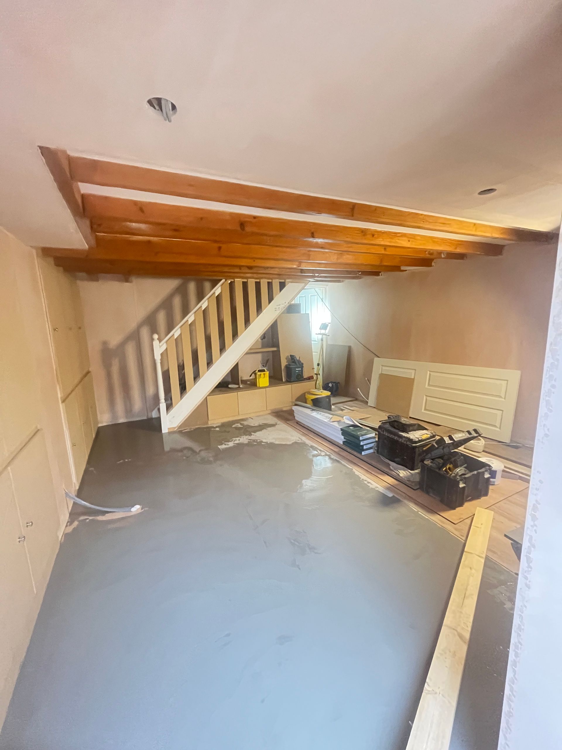 Interior with staircase under construction; gray floor, exposed beams, tools, and building materials.