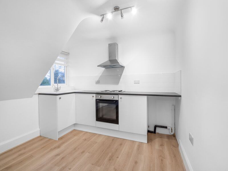 Small white kitchen with oven, cooktop, and window on angled wall.