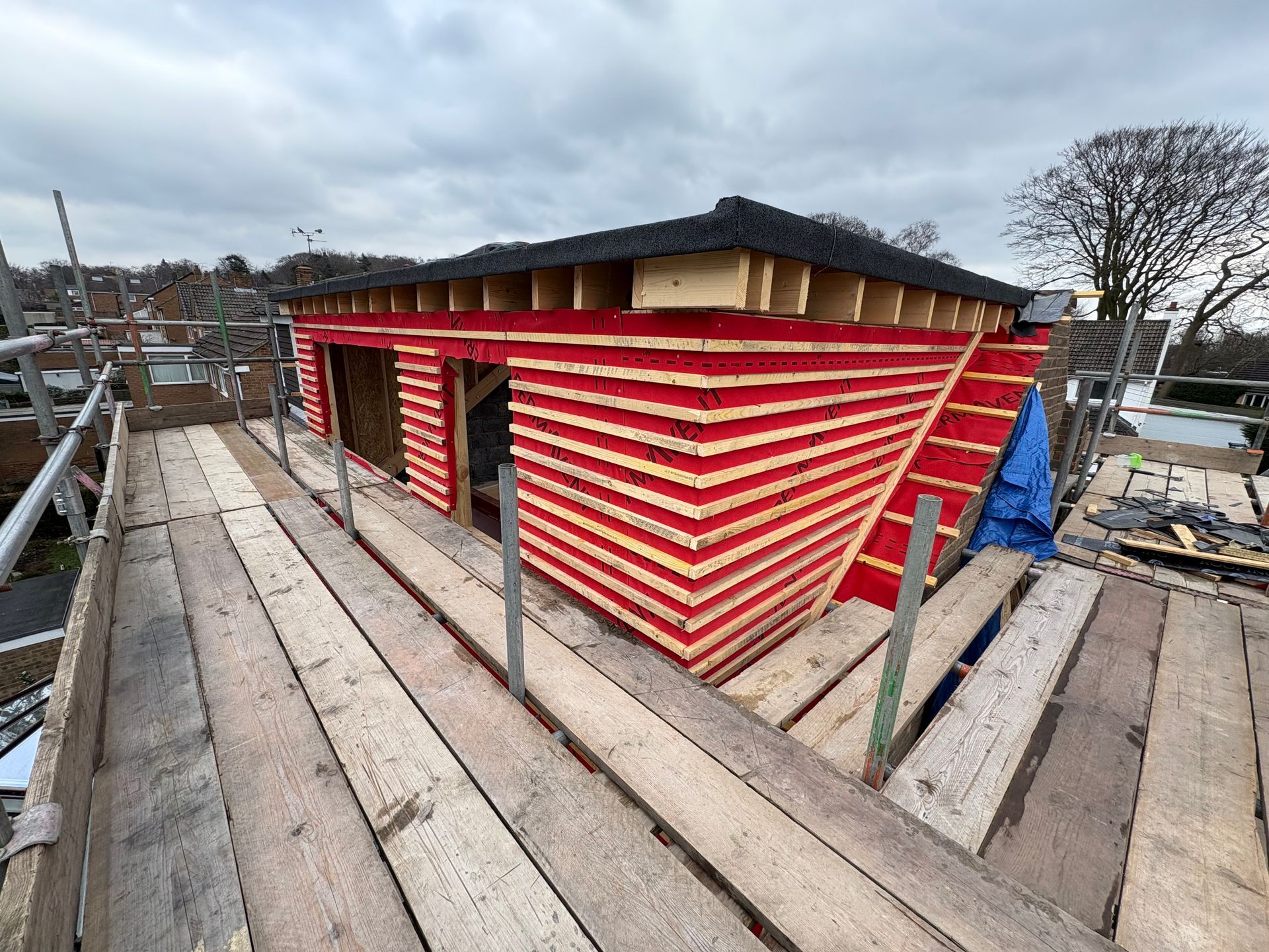 Construction of a red and wood-paneled building on a rooftop, with scaffolding in view.