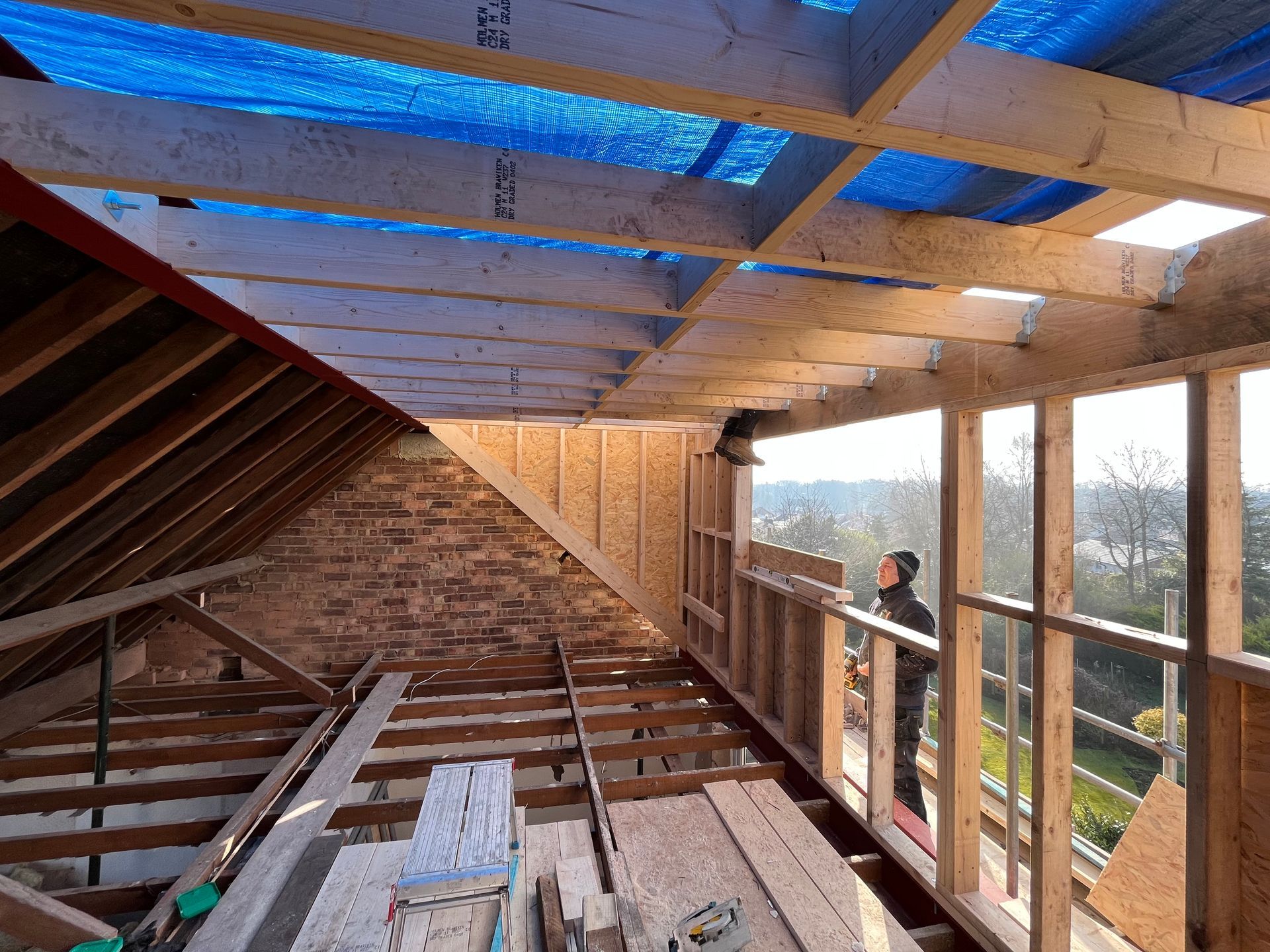 Construction in progress: attic with exposed beams, brick wall, wood framing, and a person standing.