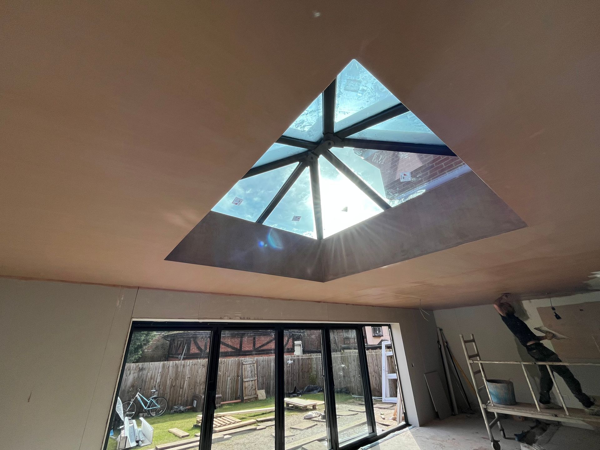 Interior view with a large triangular skylight. Light streams through. A sliding glass door and a ladder are in view.