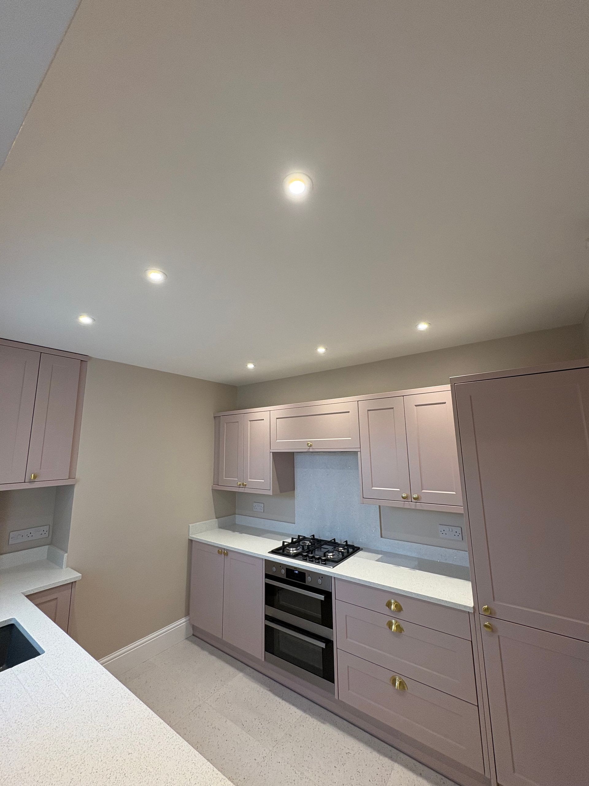 Pale pink kitchen with white countertops, silver appliances, and recessed lighting.