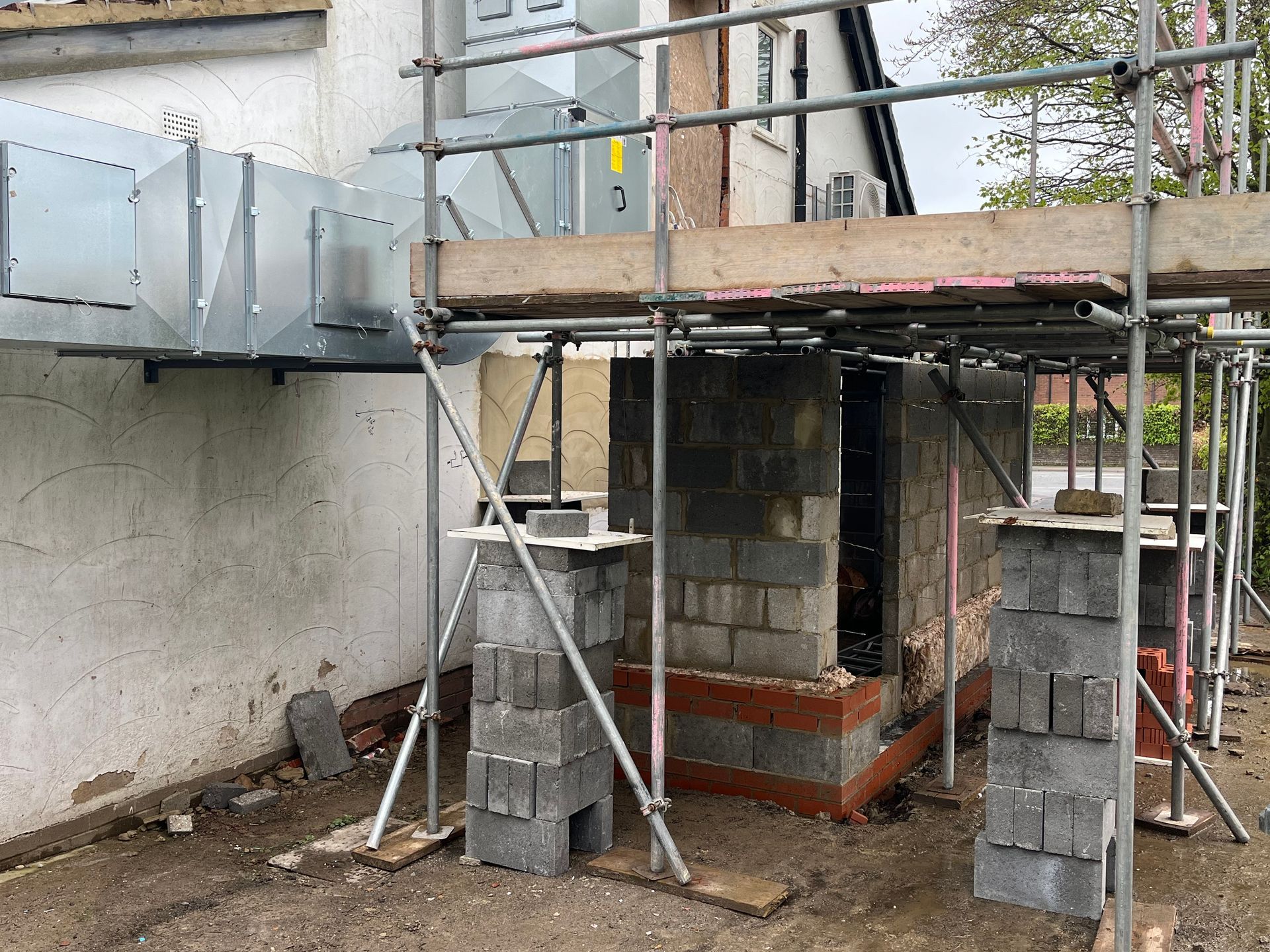 Construction site: Scaffolding around a partially built brick structure, with a metal ventilation.