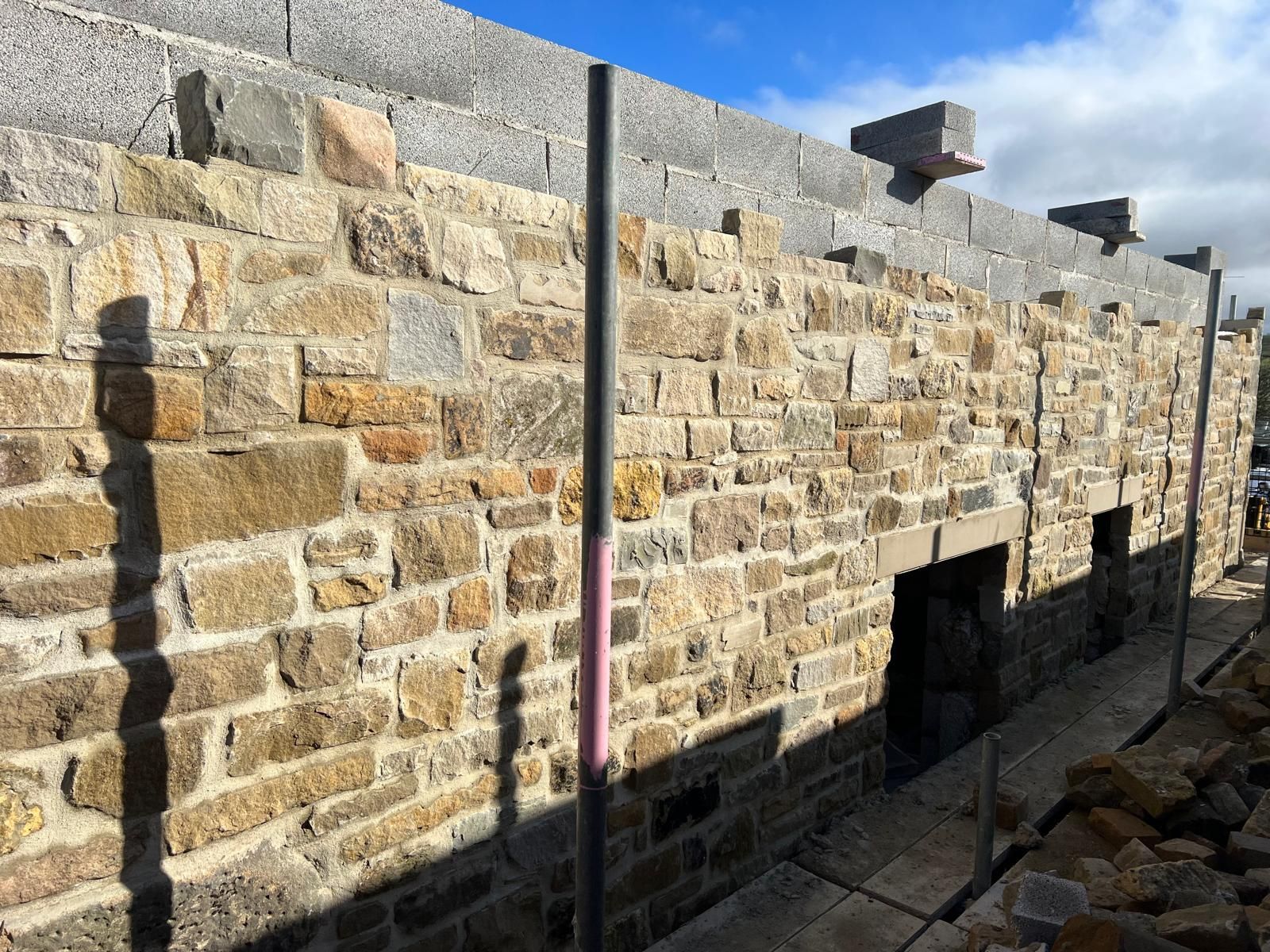 Stone wall construction with open doorways, gray blocks on top, under a blue sky.