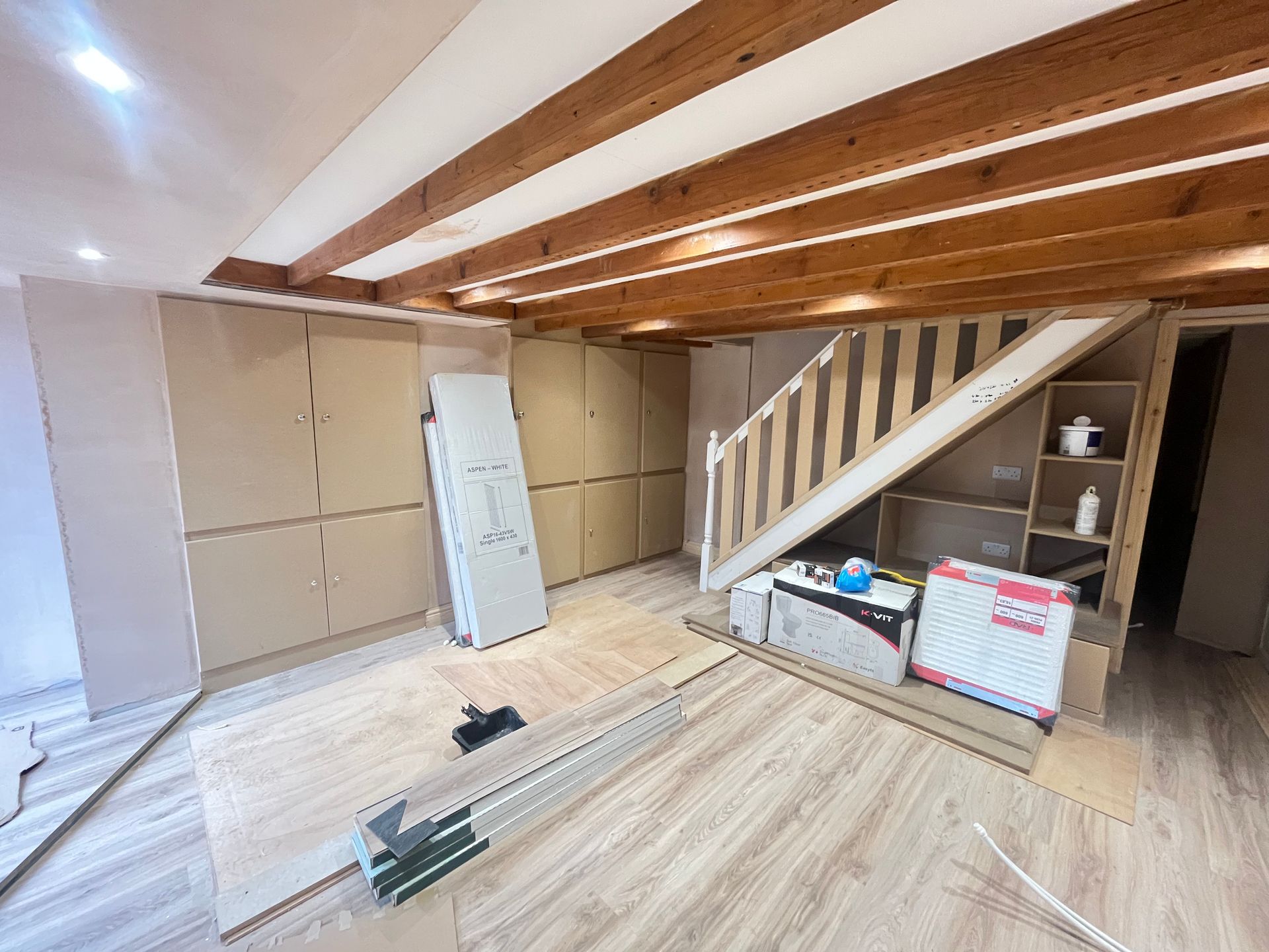 Interior under stairs with wooden beams, built-in closets, and wooden floor under construction.