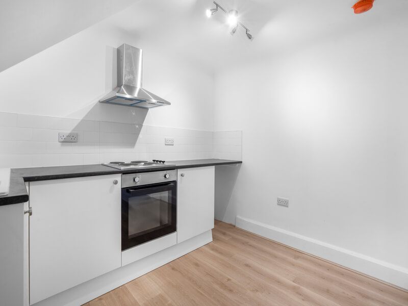 White kitchen with oven, stove, and stainless steel range hood against white walls and wood floor.