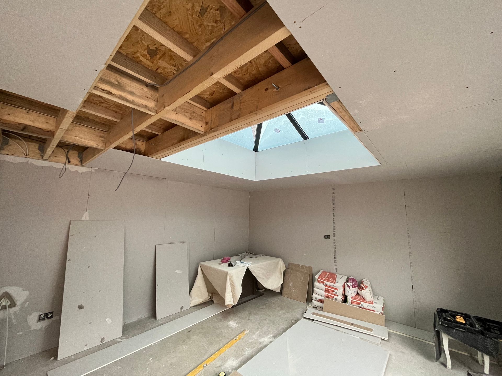 Room under construction, with a skylight, drywall, and exposed ceiling beams.