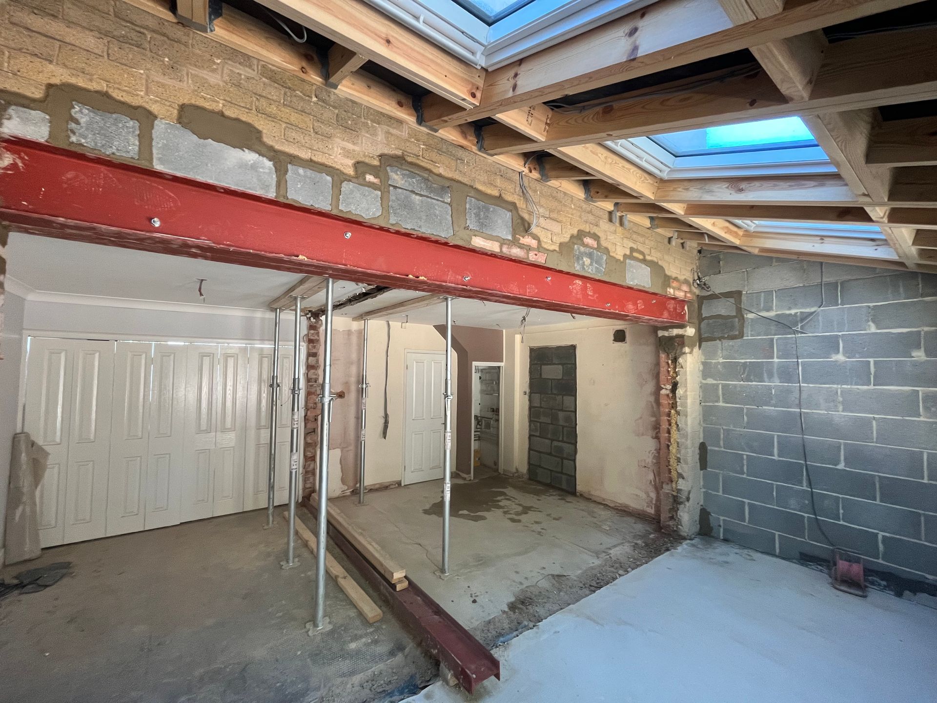 Interior construction site with red steel beam, concrete blocks, and temporary support.