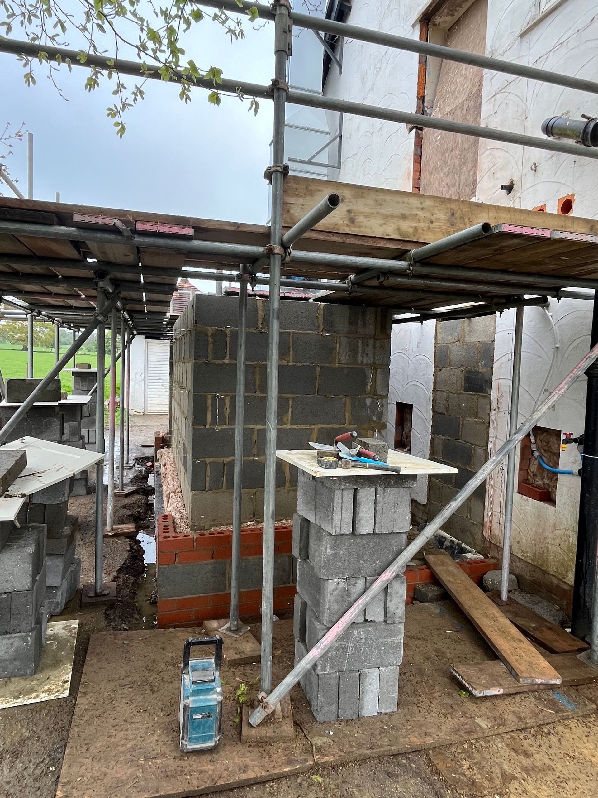 Construction site: brick structure under scaffolding. Grey blocks and orange bricks. Cloudy sky.