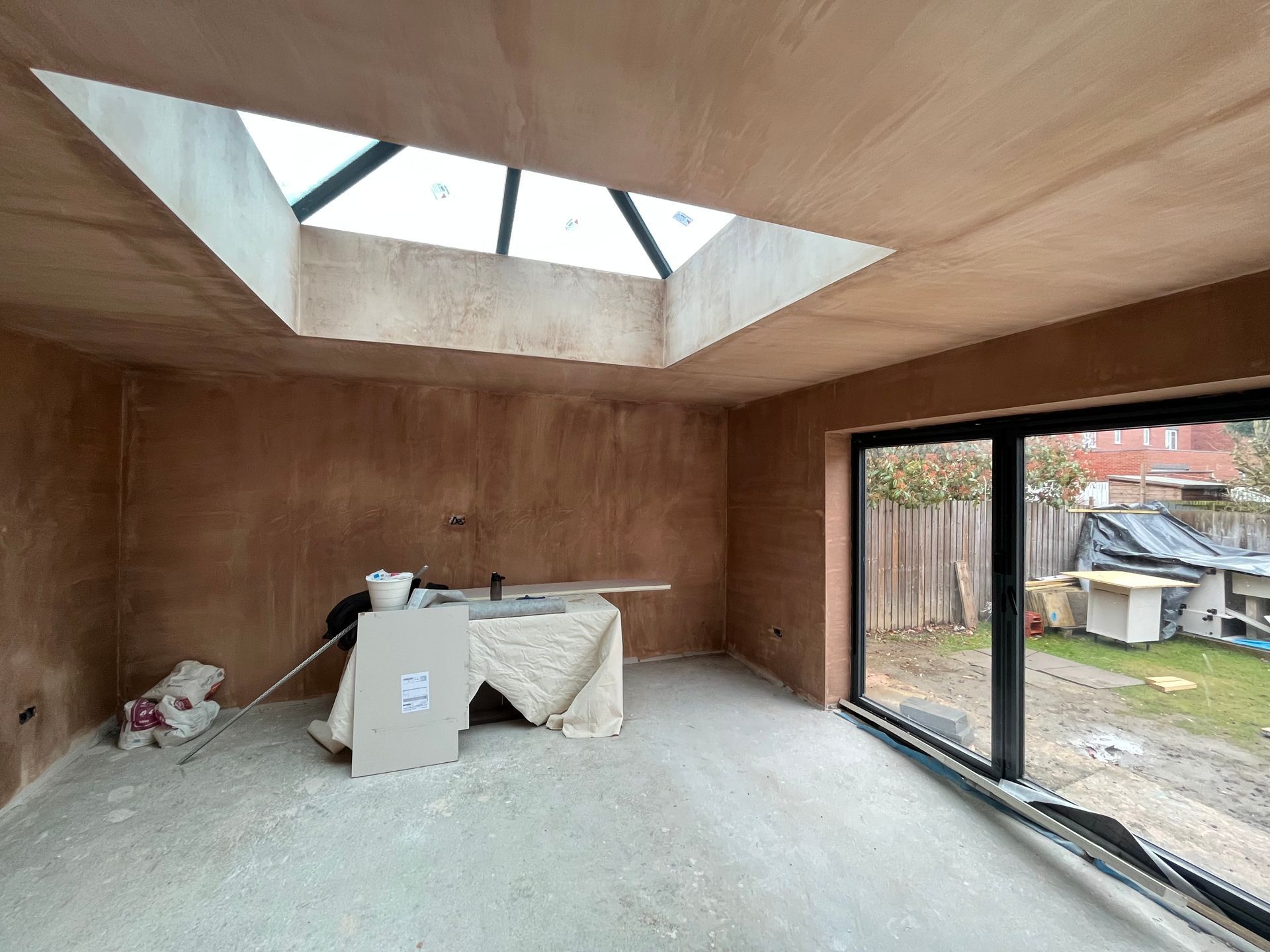 Interior of a room under construction with a skylight, bare walls, and a view of the backyard.