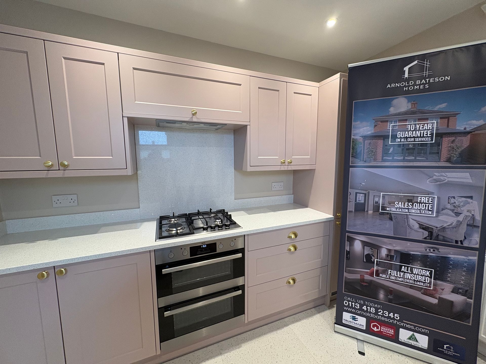 Pink kitchen with white countertops, gas stovetop, double oven, gold hardware, and promotional banner.