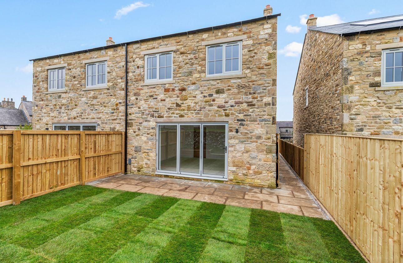 Stone-faced house with sliding glass doors and a green lawn, bordered by a wooden fence.