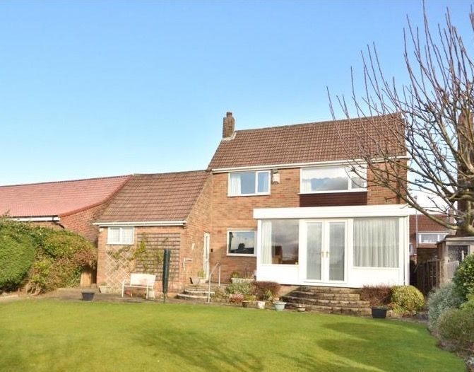 Brick house with a sunroom, on a lawn, under a blue sky.