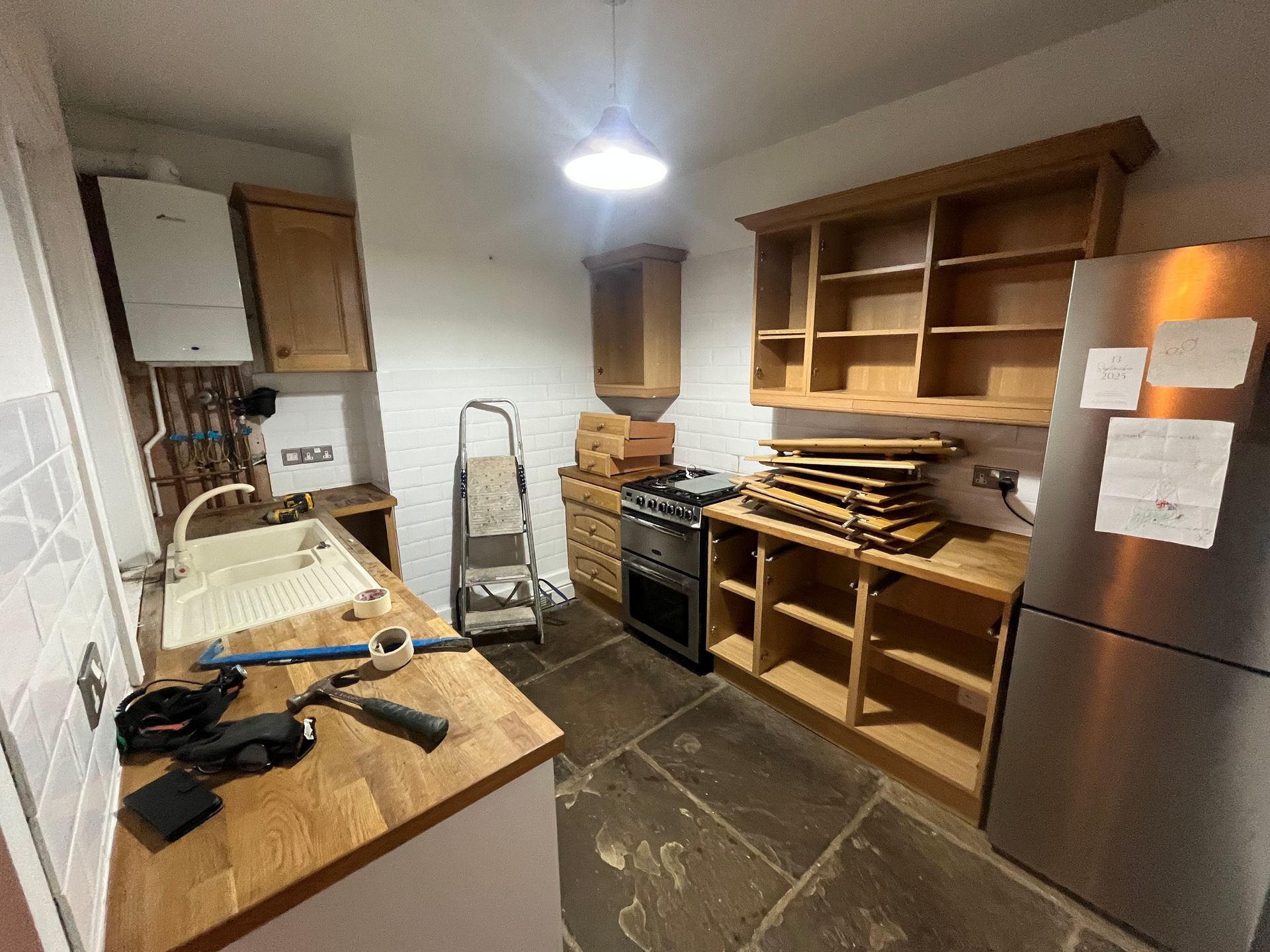 Kitchen with wooden cabinets, stove, sink, fridge, and ladder.