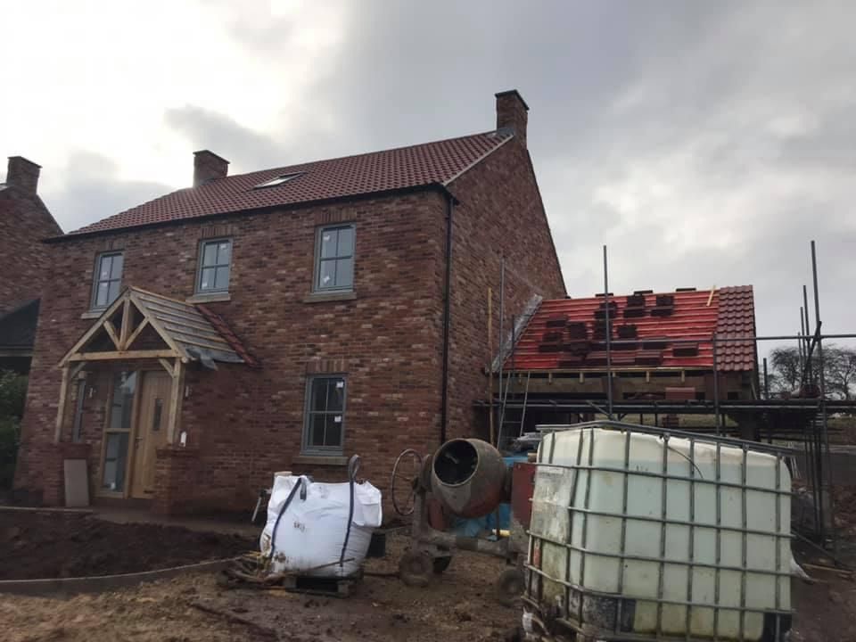 Brick house under construction with red roof tiles and construction equipment.