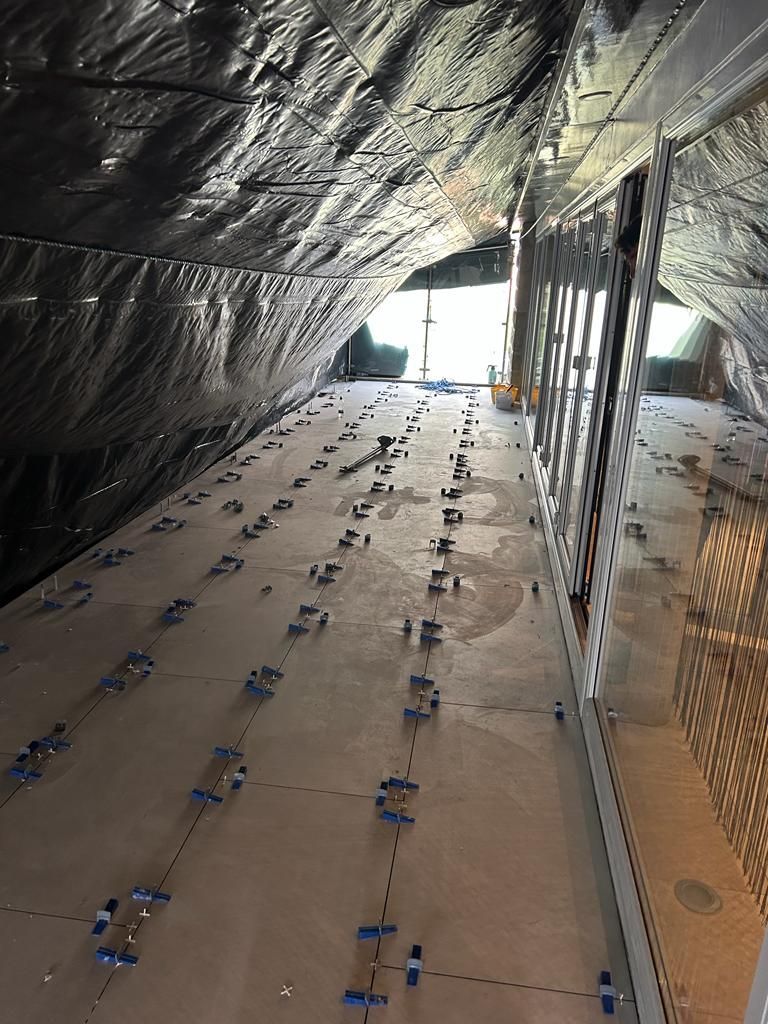 Interior view of a room with floor tile installation in progress. Gray floor with leveling clips, black covering overhead.