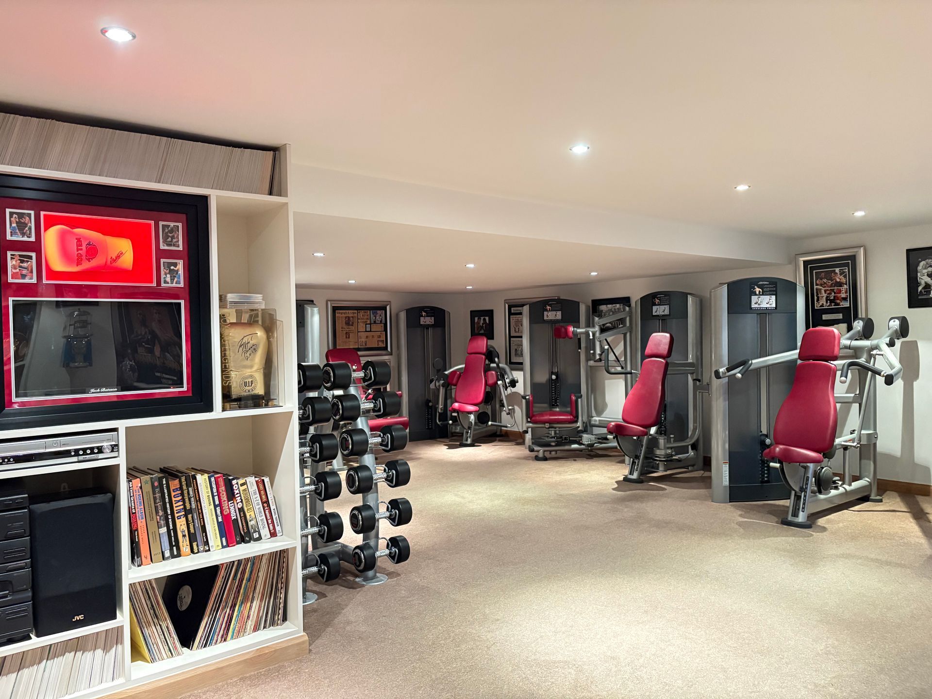 Home gym with weight racks, exercise machines, records, and framed memorabilia.