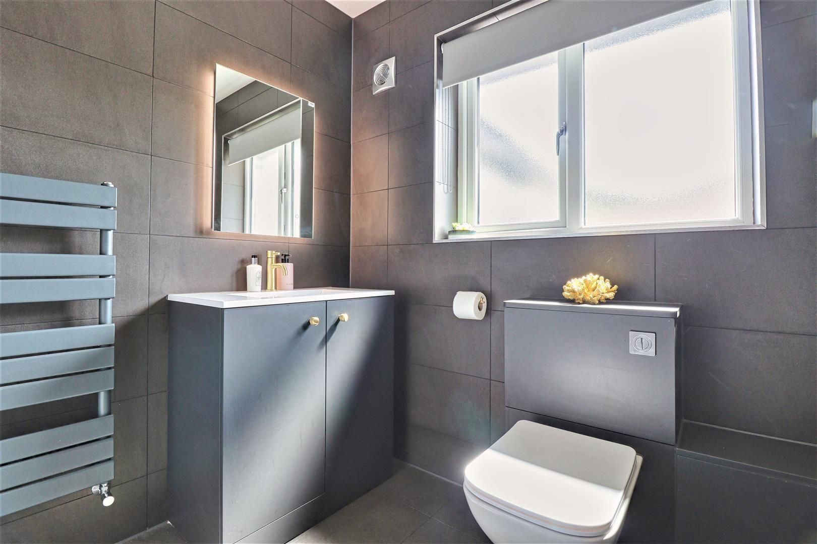 Modern gray bathroom with a toilet, vanity, towel rack, and window.