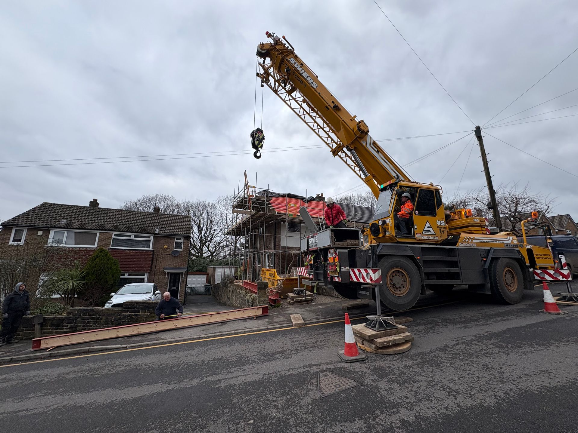 A yellow crane lifting materials at a house under construction, roadside scene. Cloudy day.