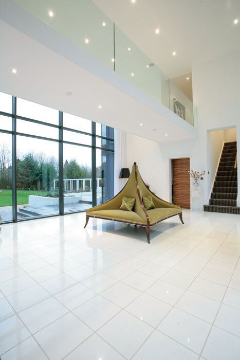 Spacious white foyer with large windows, a unique green sofa, and a staircase leading upstairs.