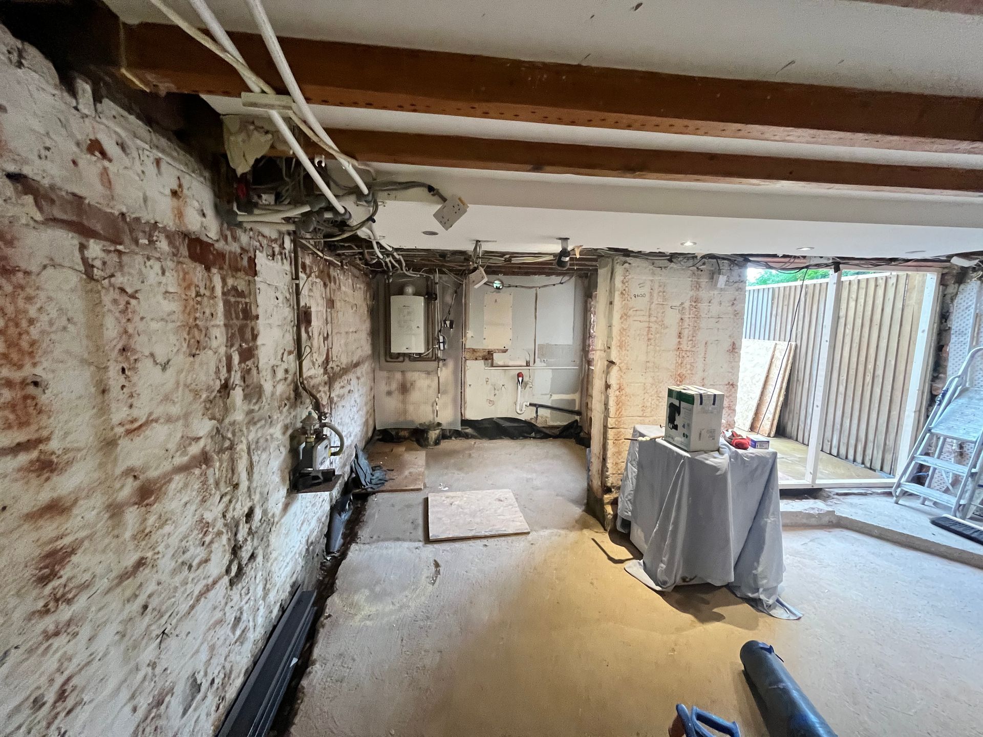 Basement undergoing renovation; exposed brick walls, utility pipes, unfinished floor, and tools.