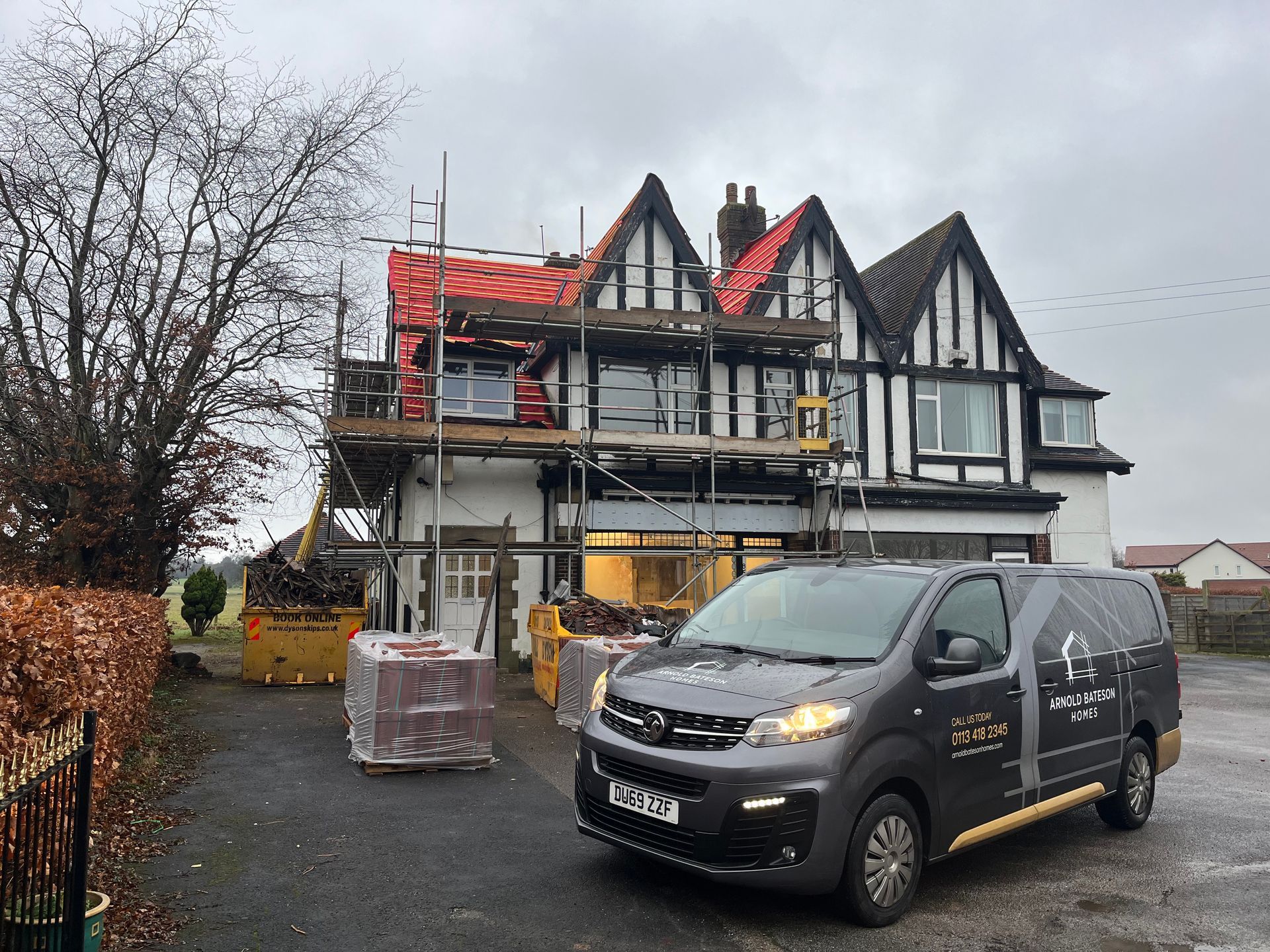 House under renovation with scaffolding, a van, and construction materials.