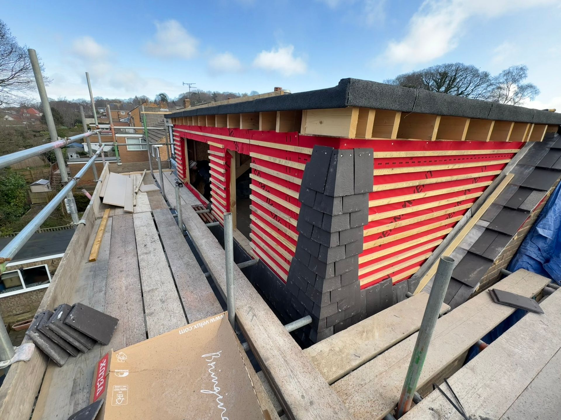 Roof construction: red-striped siding, dark gray slate, scaffolding. Sunny outdoor setting.