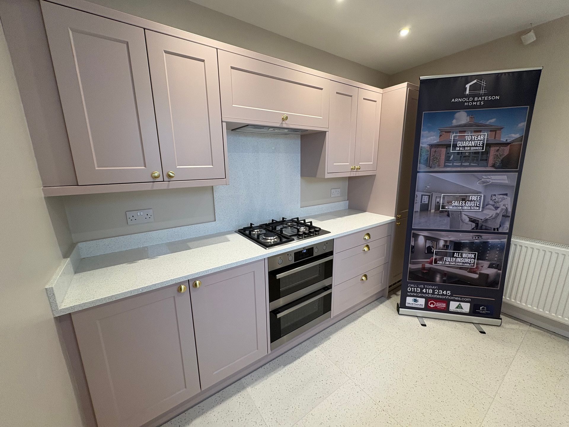 Pink kitchen cabinets with a white countertop, gas stove, and oven. A banner stands to the right.