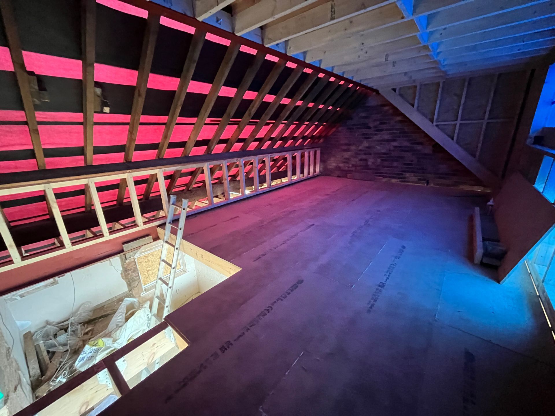 Attic room under construction with exposed rafters, new flooring, and a partially framed wall.