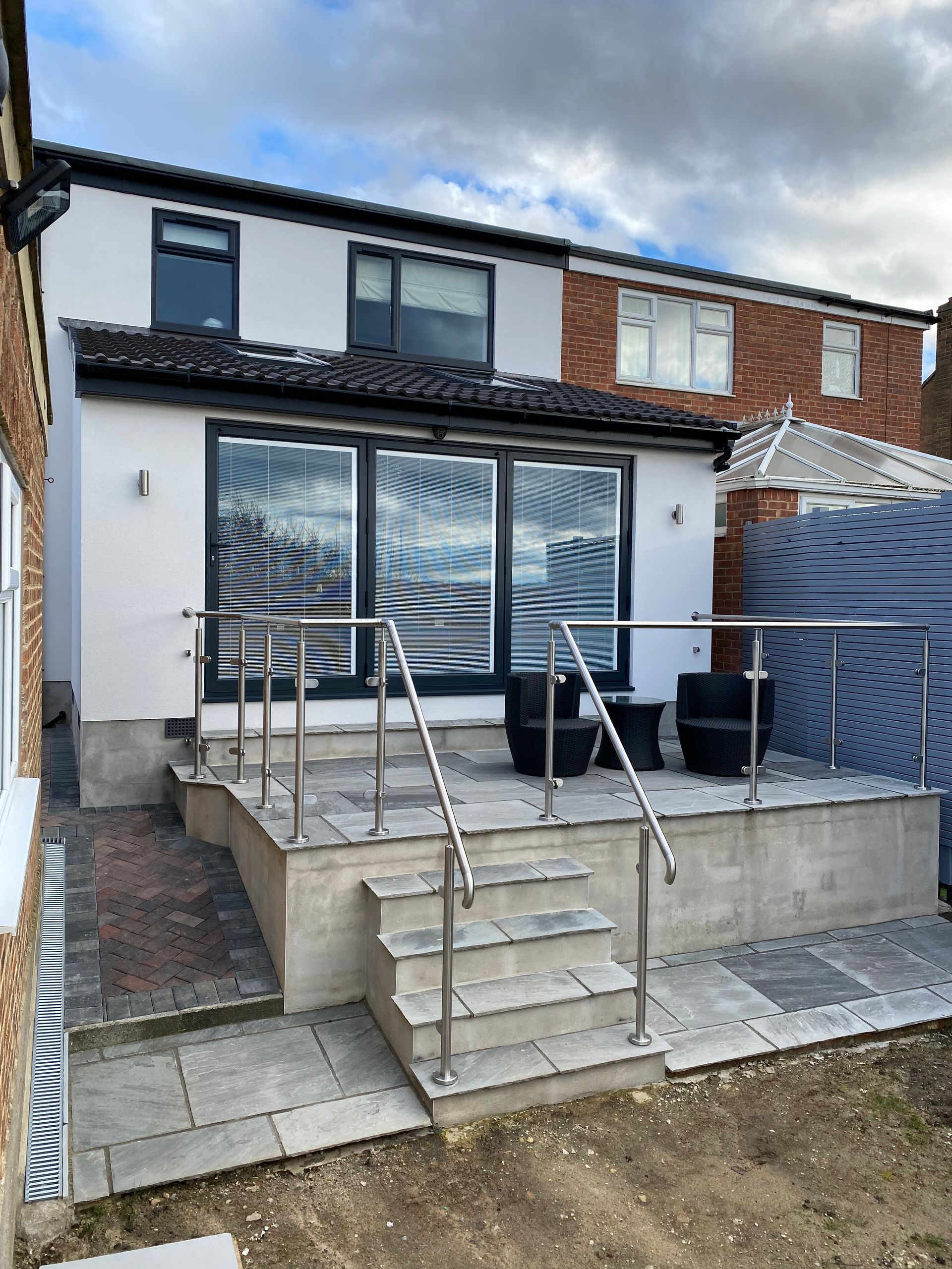 Back of a house with a raised patio, steps, and a railing, exterior, with modern gray and white finishes.