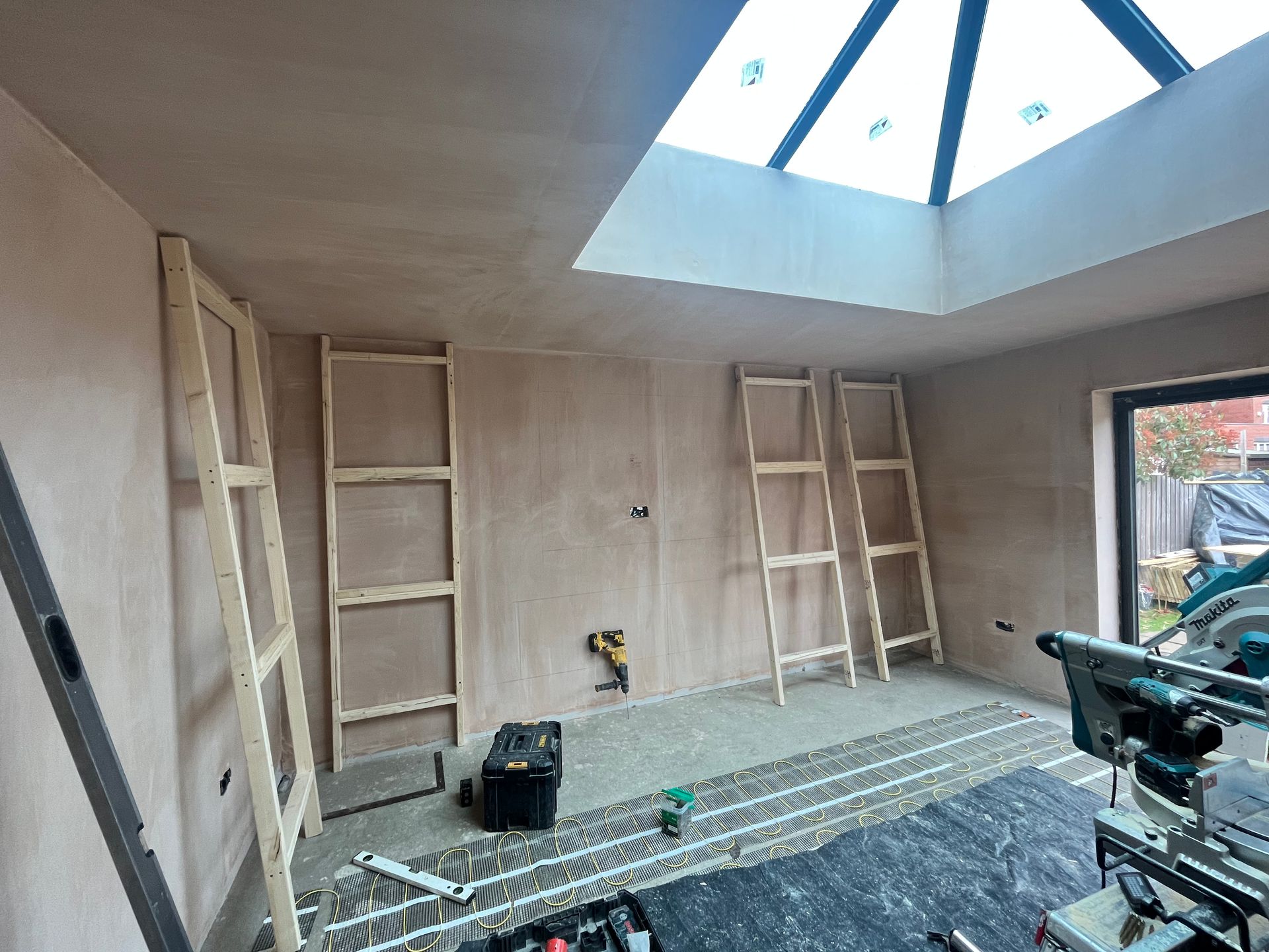 Room renovation in progress, featuring wooden frames on walls, a skylight, and construction tools.