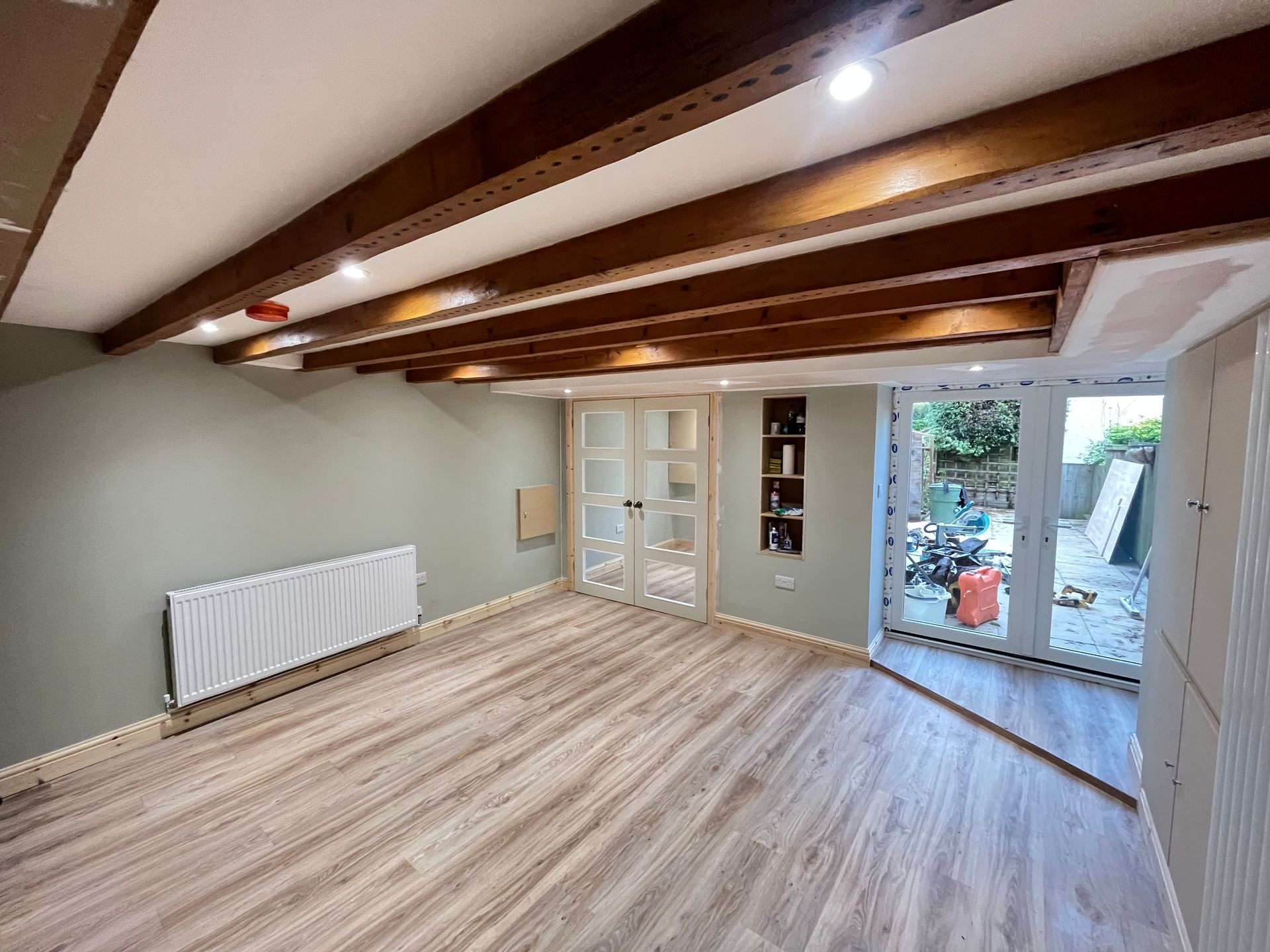 Room interior with light wood floors, sage green walls, and dark wood beams on the ceiling.