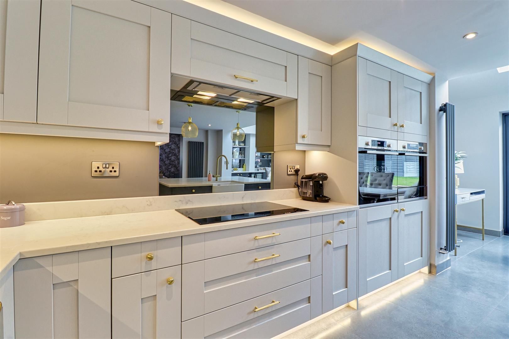 Modern kitchen with light gray cabinets, gold hardware, and mirrored backsplash.