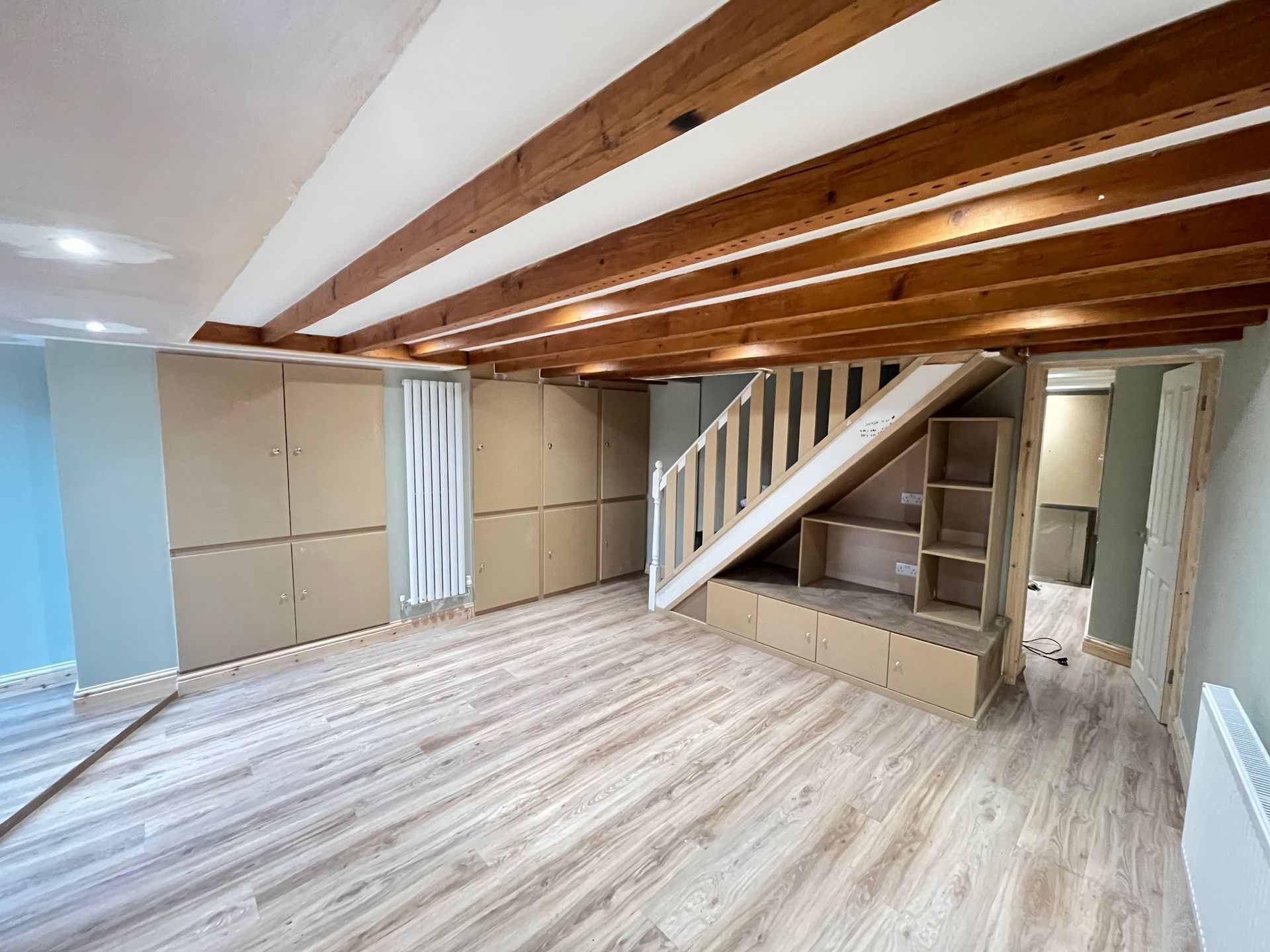 Interior renovation with wood beams, stairs, and storage cabinets. Light wood flooring and blue-green walls.