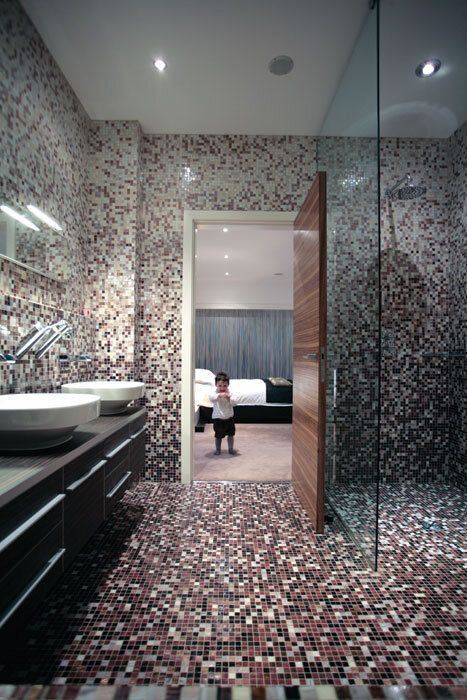 Bathroom with mosaic tile walls and floor, a child stands in doorway to bedroom.