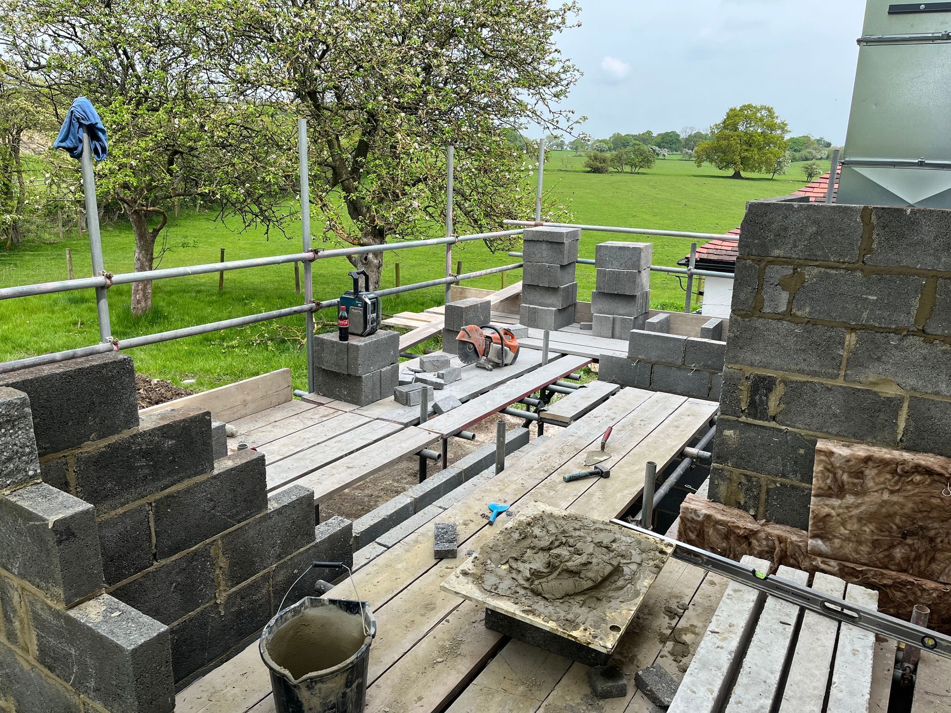 Construction site with cinder block walls and scaffolding, set against a green field background.