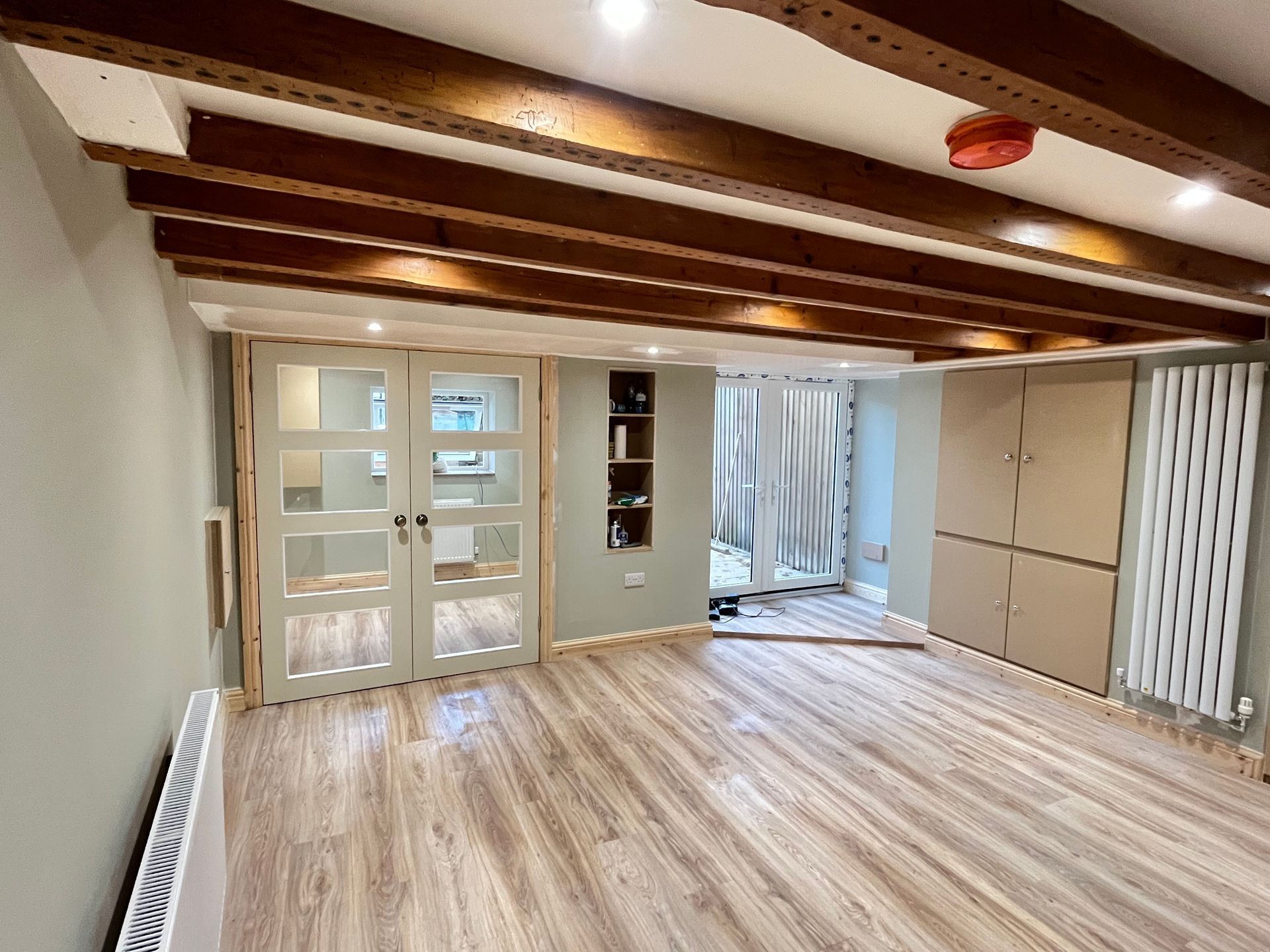 Room interior with wood beams, light wood floor, and double glass doors; neutral colors.